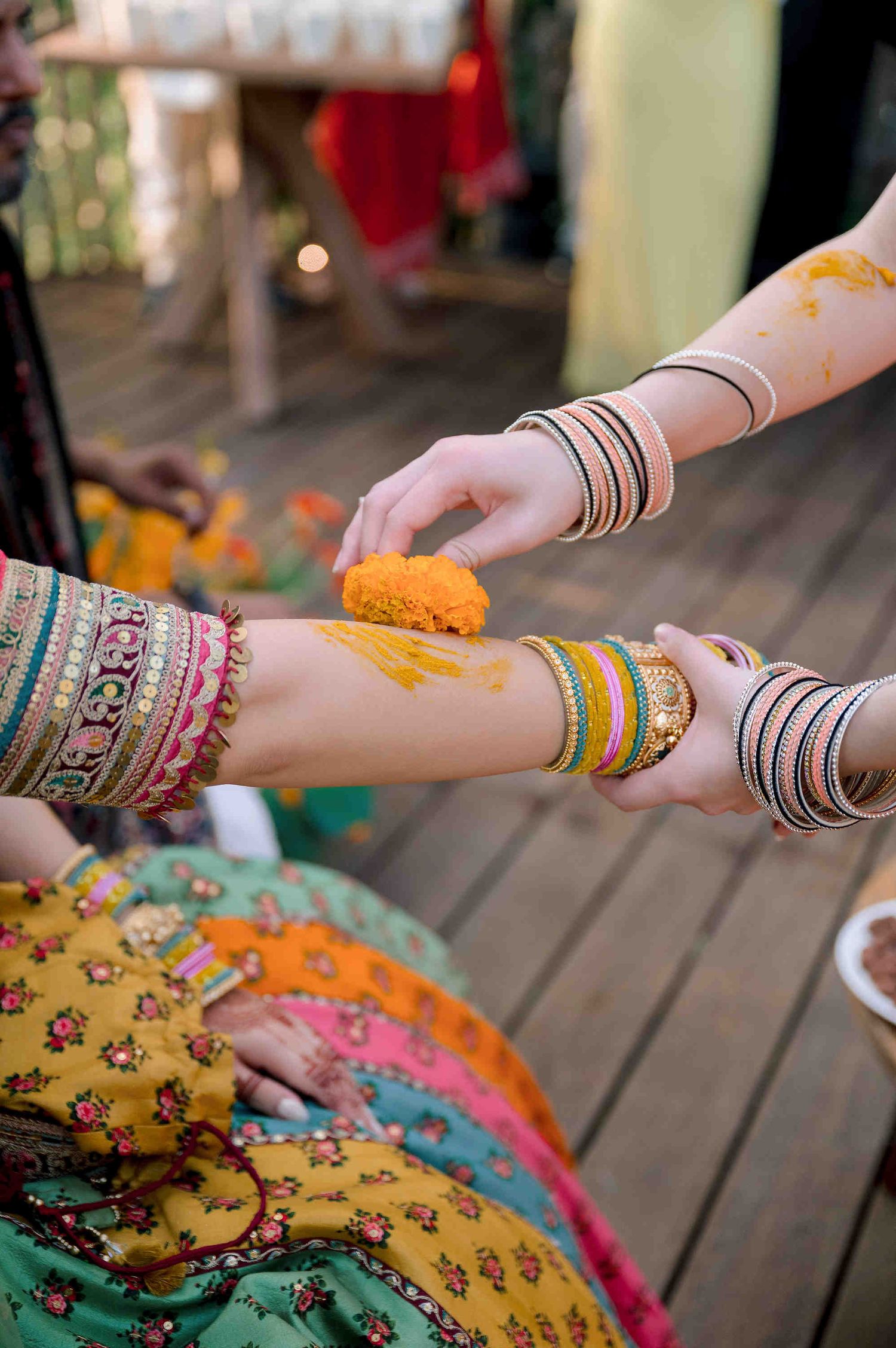 Haldi ceremony with women in colorful bangles applying turmeric paste on hands during Indian wedding ritual.