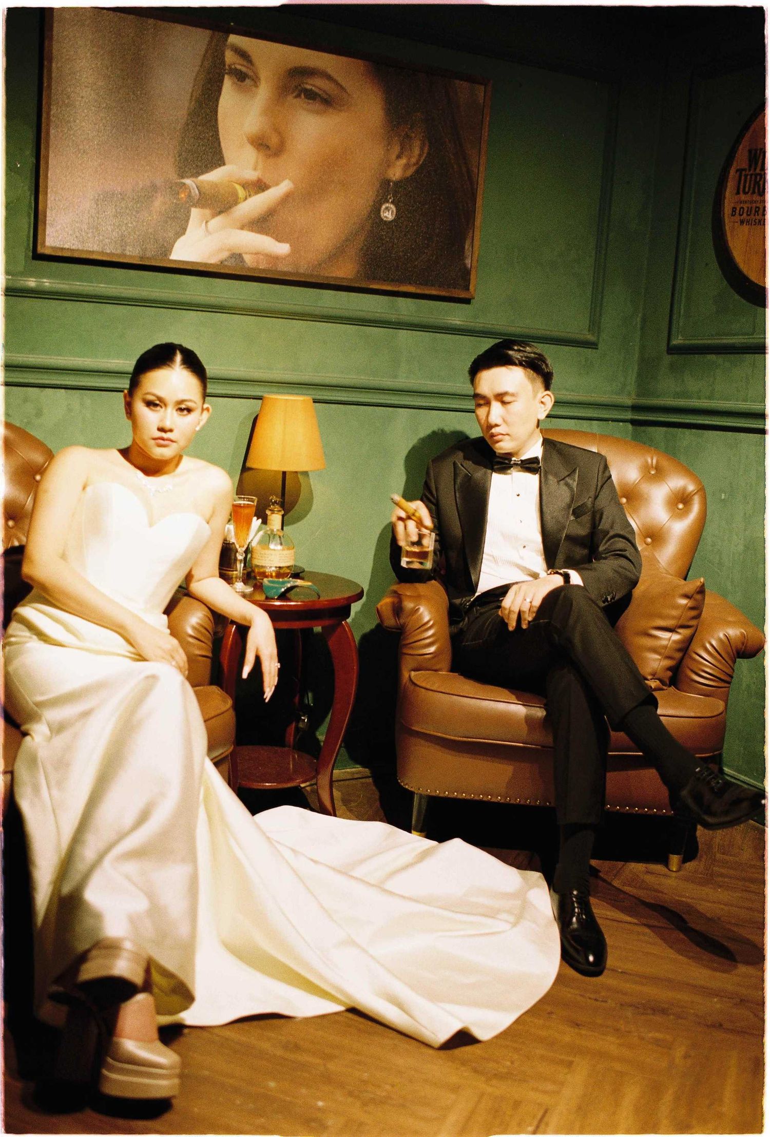 Vietnam pre-wedding: formal couple relaxing in leather armchairs with vintage decor and mood lighting, by AnhVuWedding.