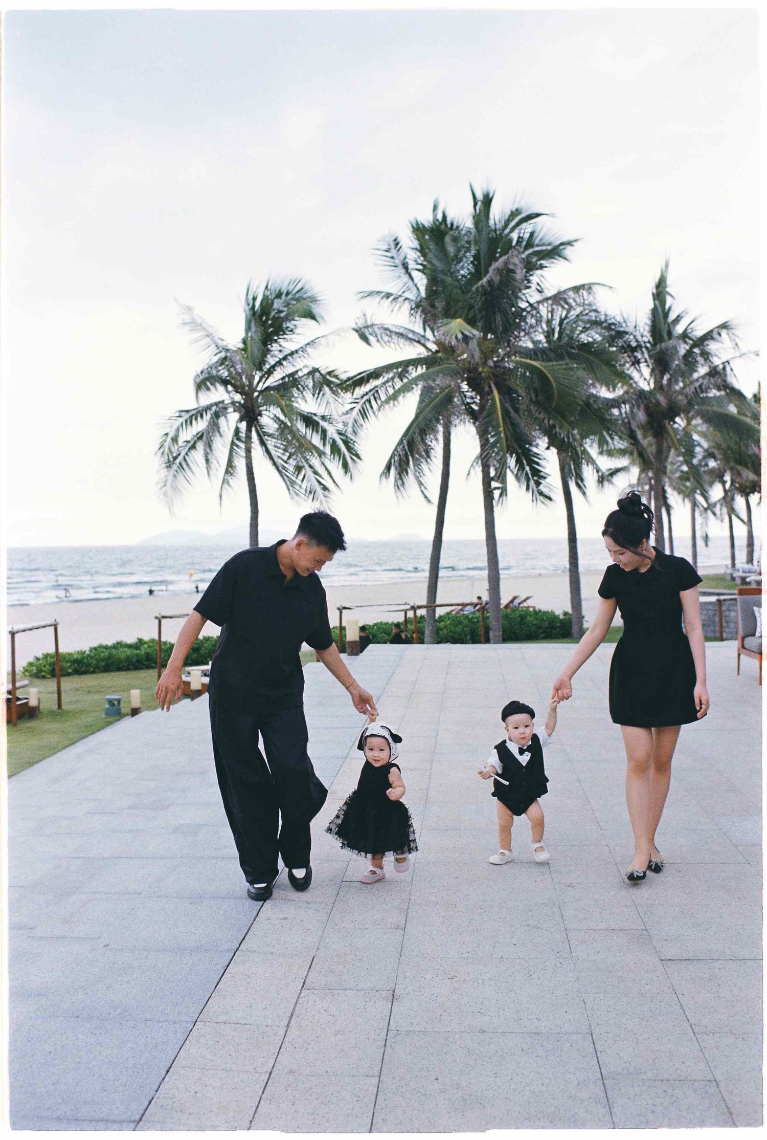 Da Nang family: family takes a stroll along a beachfront path lined with palm trees, by AnhVuWedding.