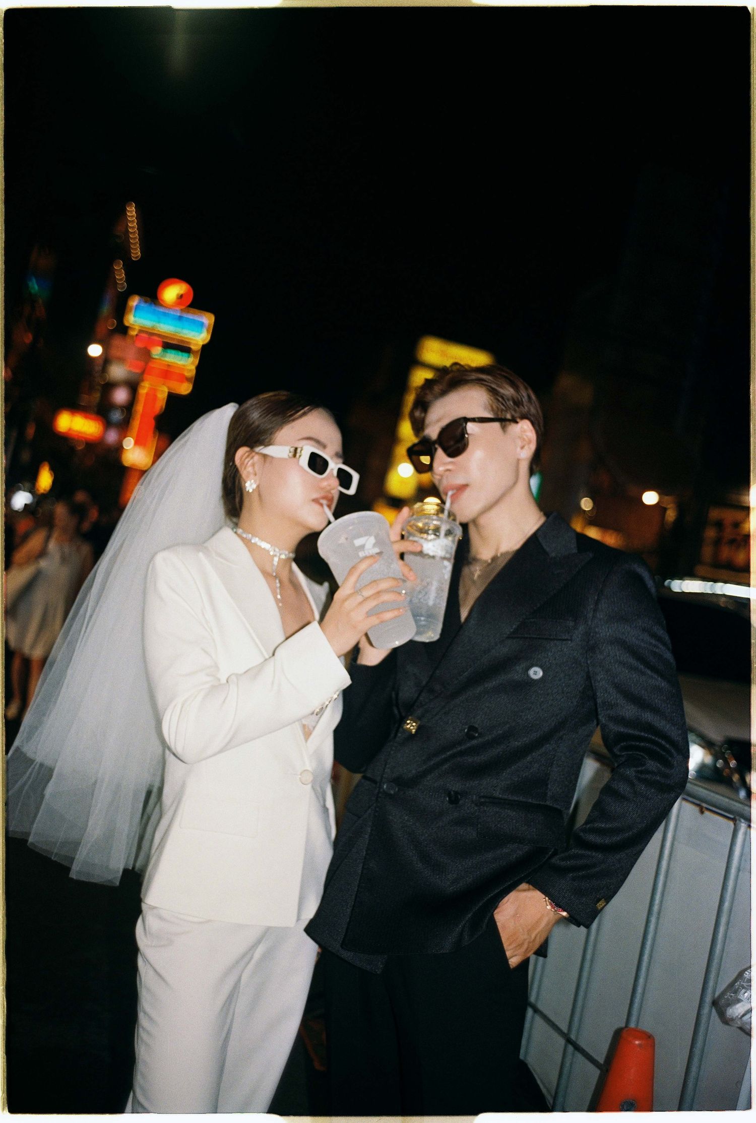 Saigon pre-wedding: two people in contrasting outfits interact playfully on a nighttime street with neon signs, by AnhVuWedding.