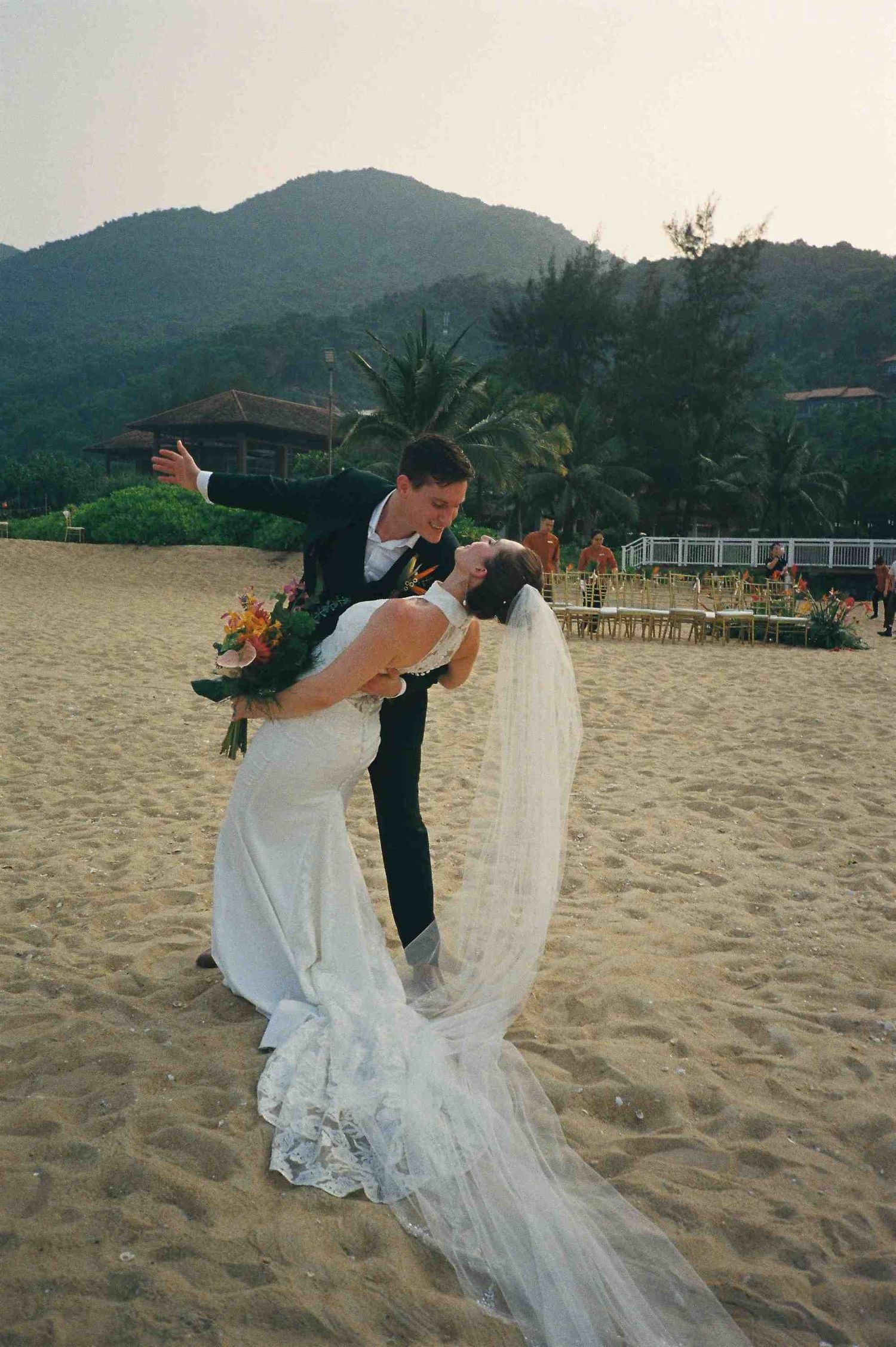 Lang Co wedding: couple in wedding attire performs a dramatic dip pose on a sandy beach, by AnhVuWedding.