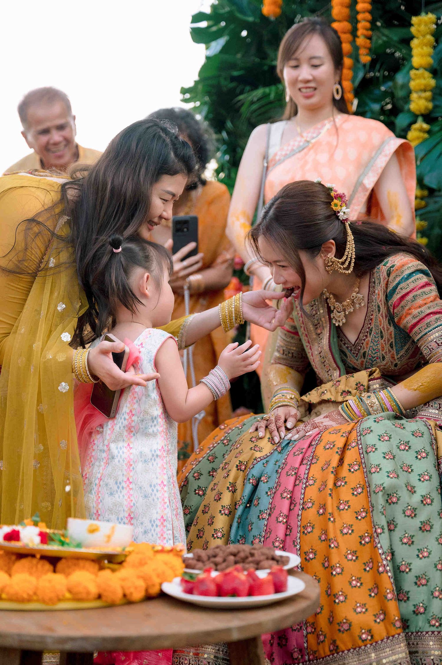 A bride in colorful Indian lehenga receives sweets from a little girl during a traditional wedding ceremony.