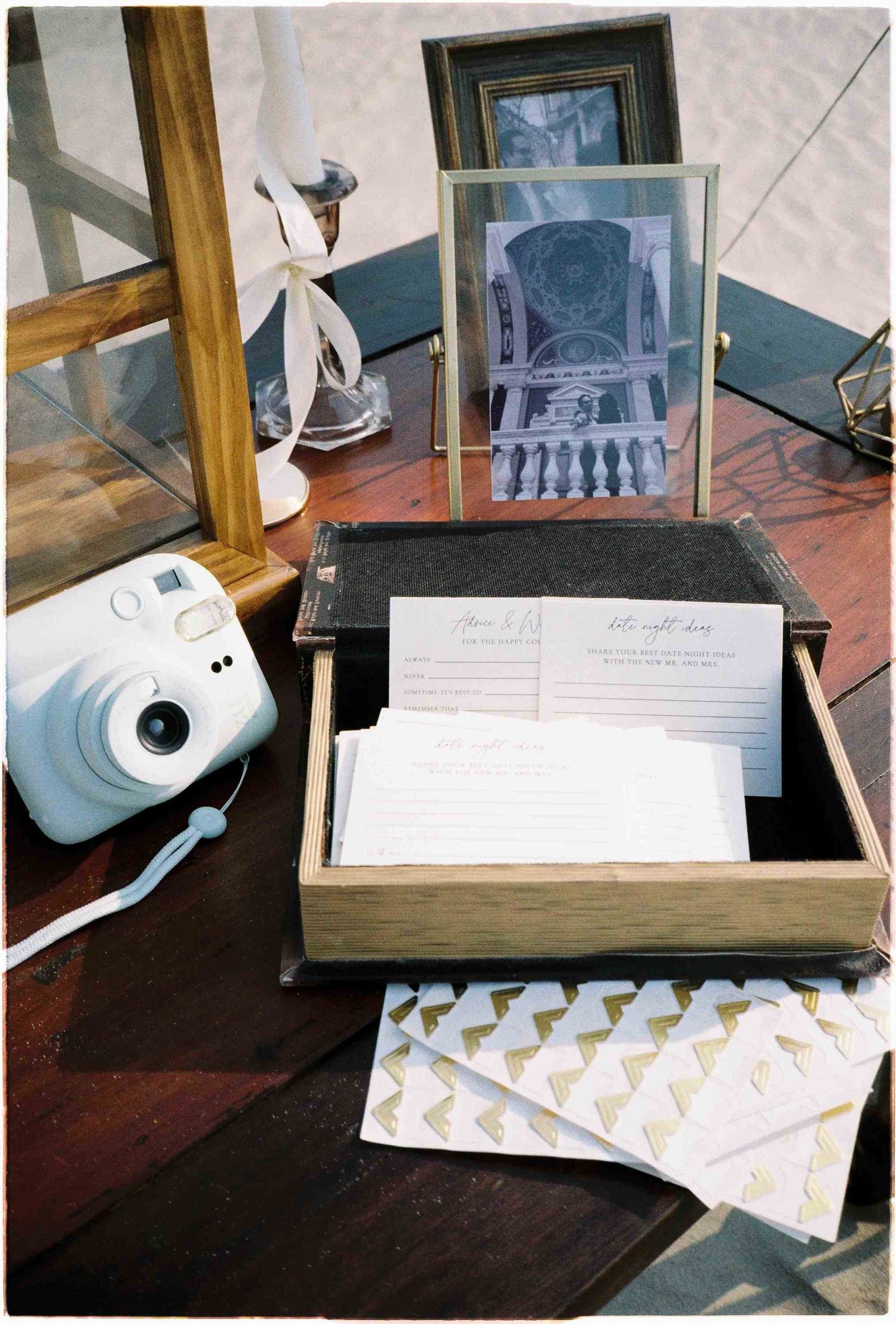Wedding guest book box with cards, Instax mini camera, and framed black and white photo on a wooden table.