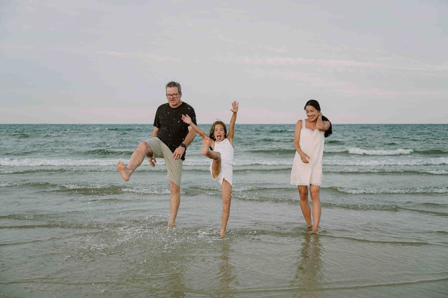 Da Nang family: family enjoys a playful moment together at the beach as waves roll in during sunset, by AnhVuWedding.