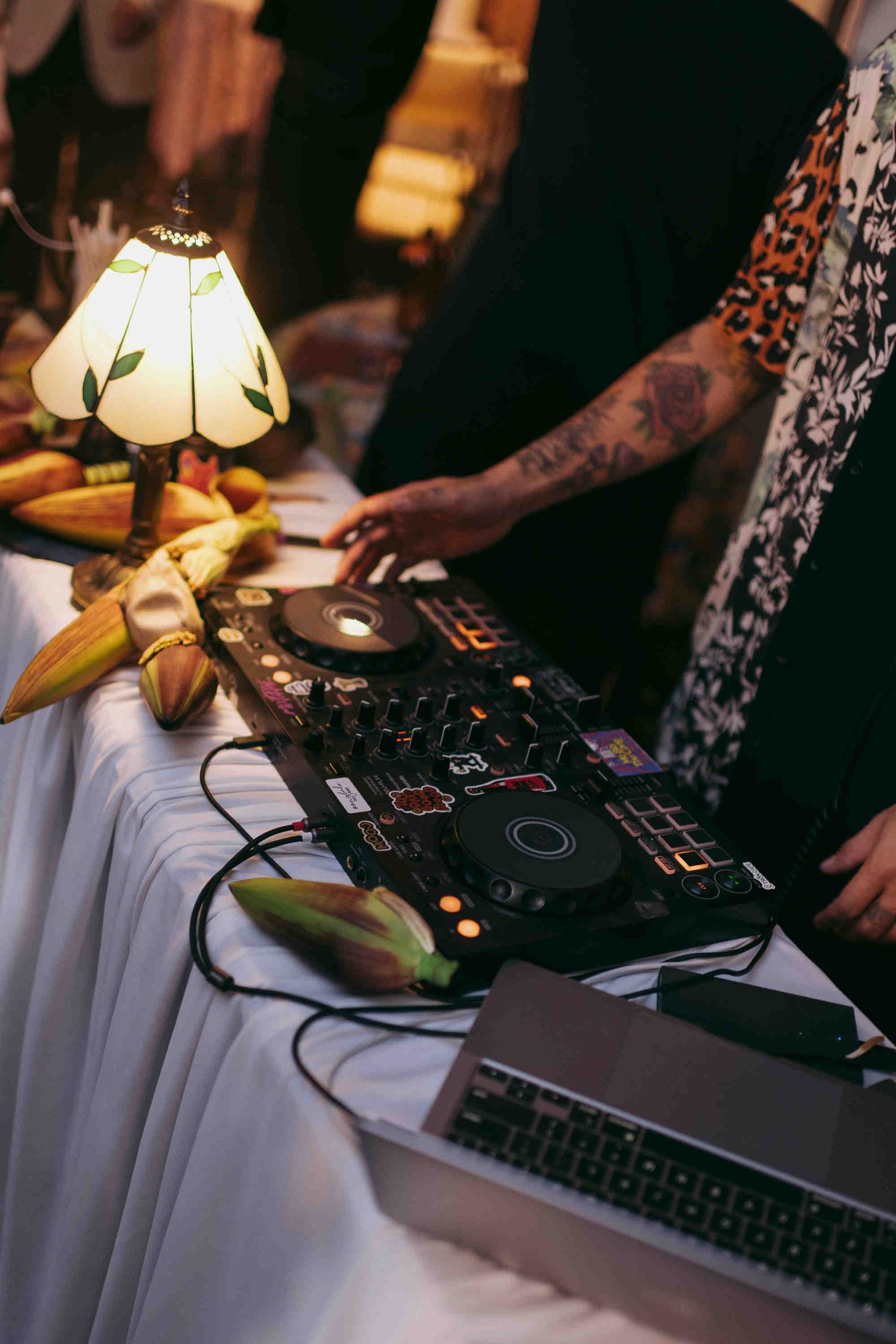 DJ mixing music on Pioneer decks at an event with a vintage lamp and tropical fruit decorations.