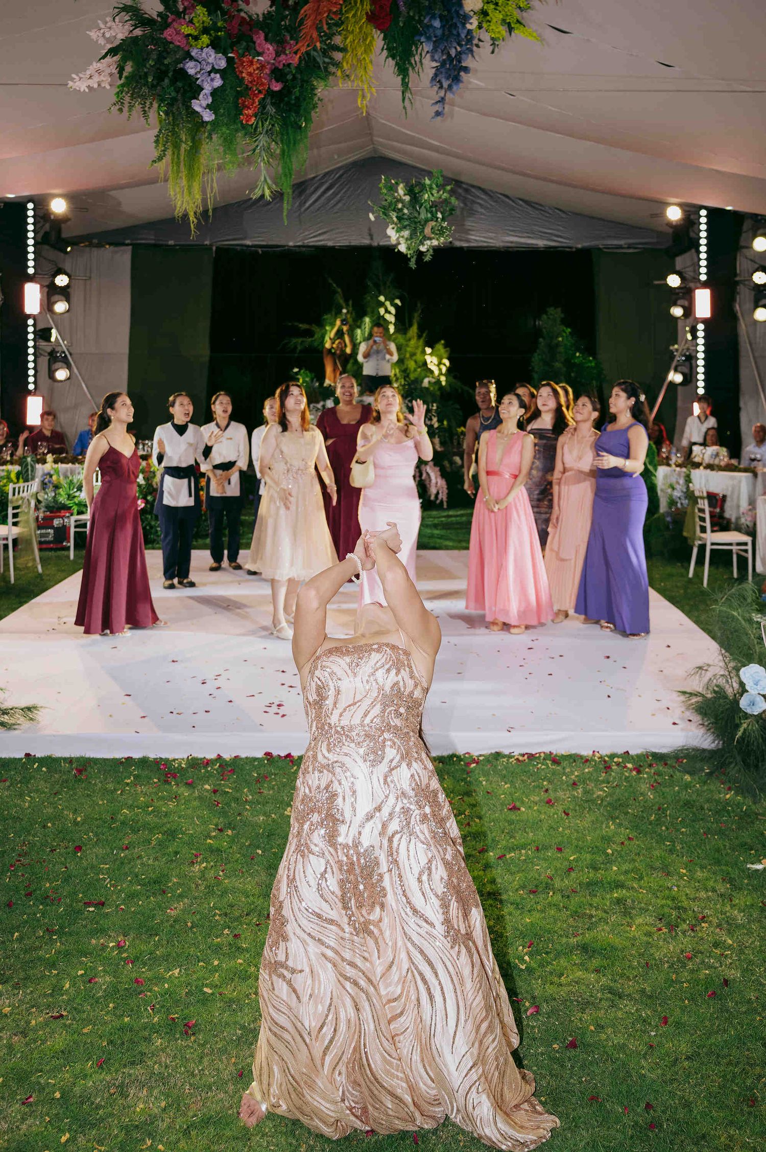 Bride in gold gown tossing bouquet to bridesmaids in colorful dresses at decorated wedding reception.