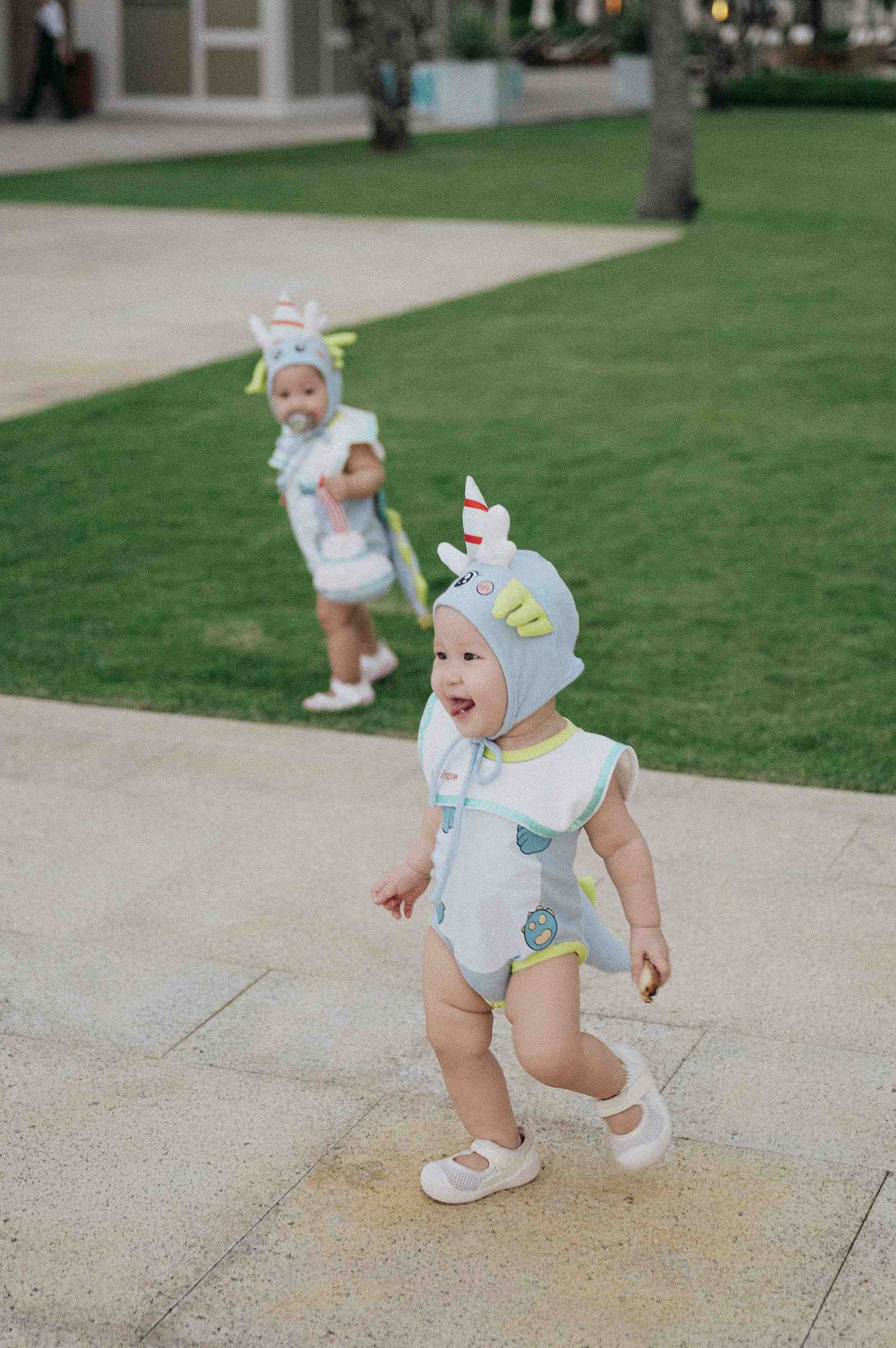 Da Nang family: baby in an adorable blue outfit takes first steps on a stone patio, by AnhVuWedding.