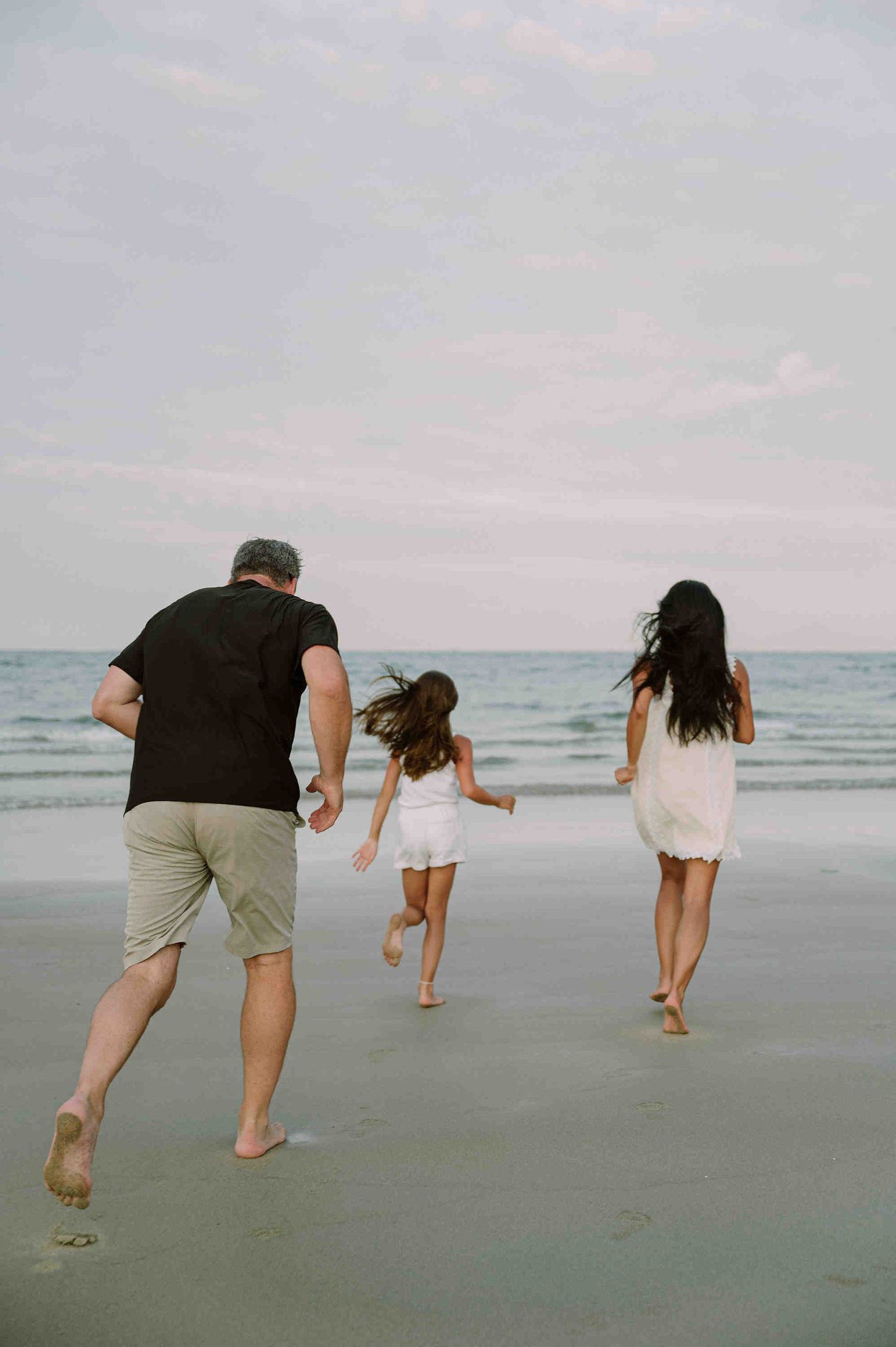 Da Nang family: people running and jumping playfully on a misty beach during an overcast day, by AnhVuWedding.