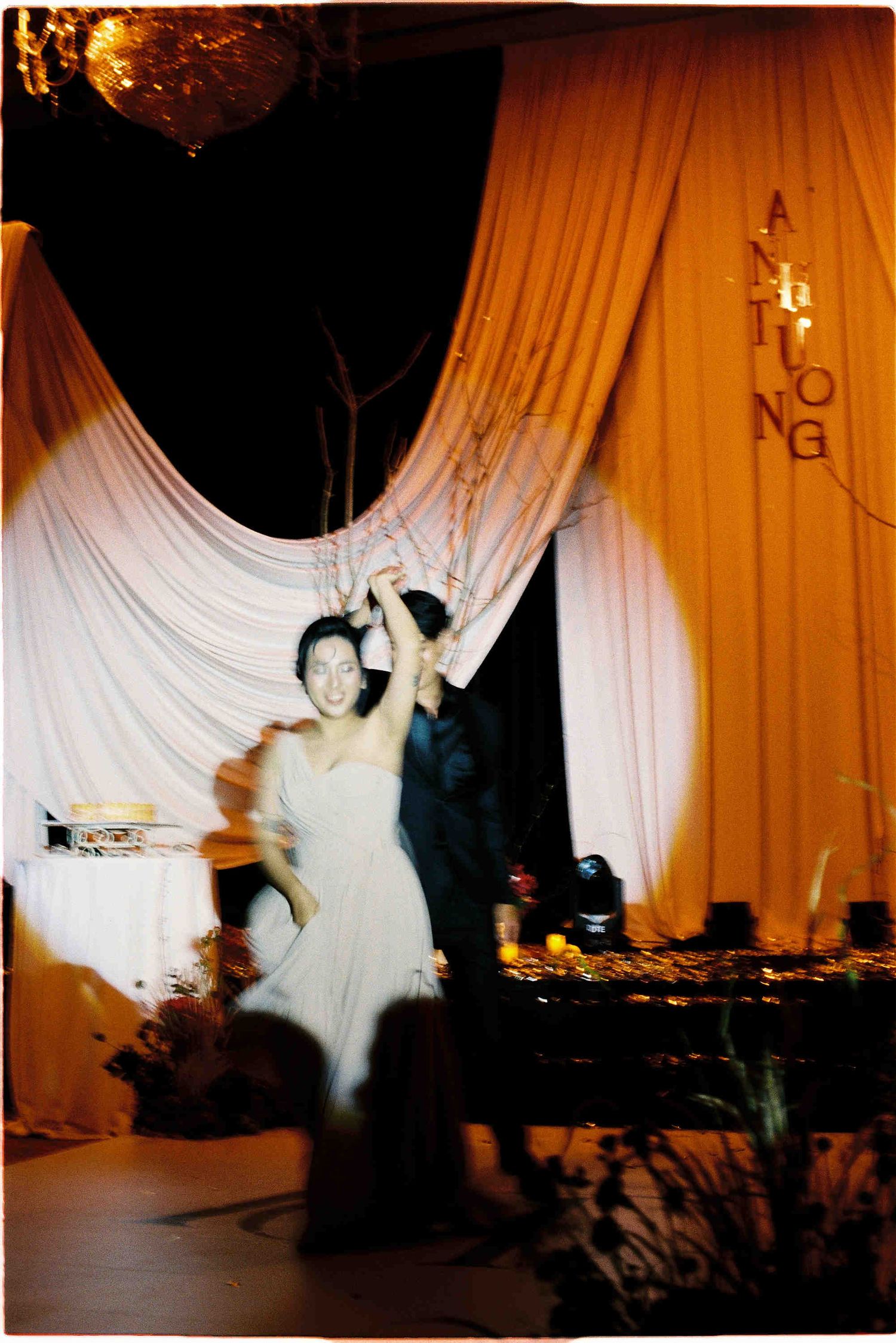 Couple sharing first dance at wedding reception with orange and white draped backdrop.