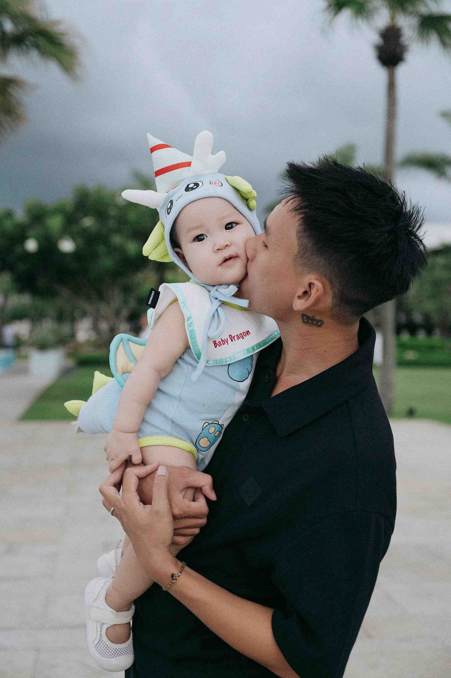 Da Nang family: tender moment between parent and baby wearing a cute animal-themed outfit outdoors, by AnhVuWedding.