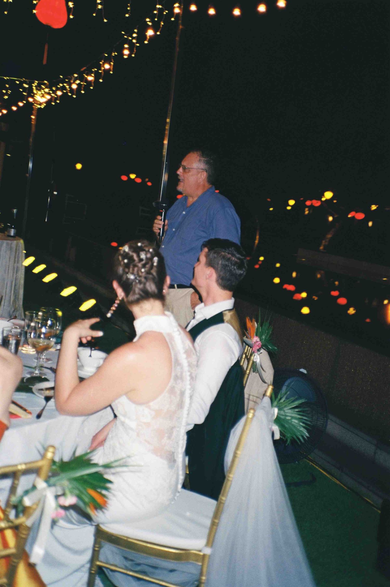 Da Nang wedding reception: man in blue shirt gives a toast speech at an outdoor evening wedding reception with string, by AnhVuWedding.