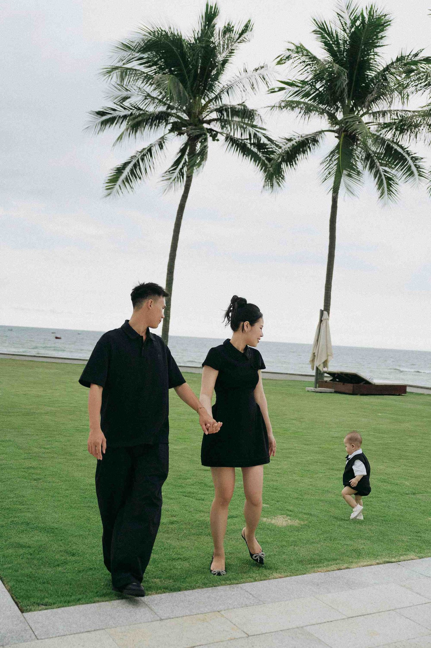 Da Nang family: couple walking along a beachfront path, by AnhVuWedding.