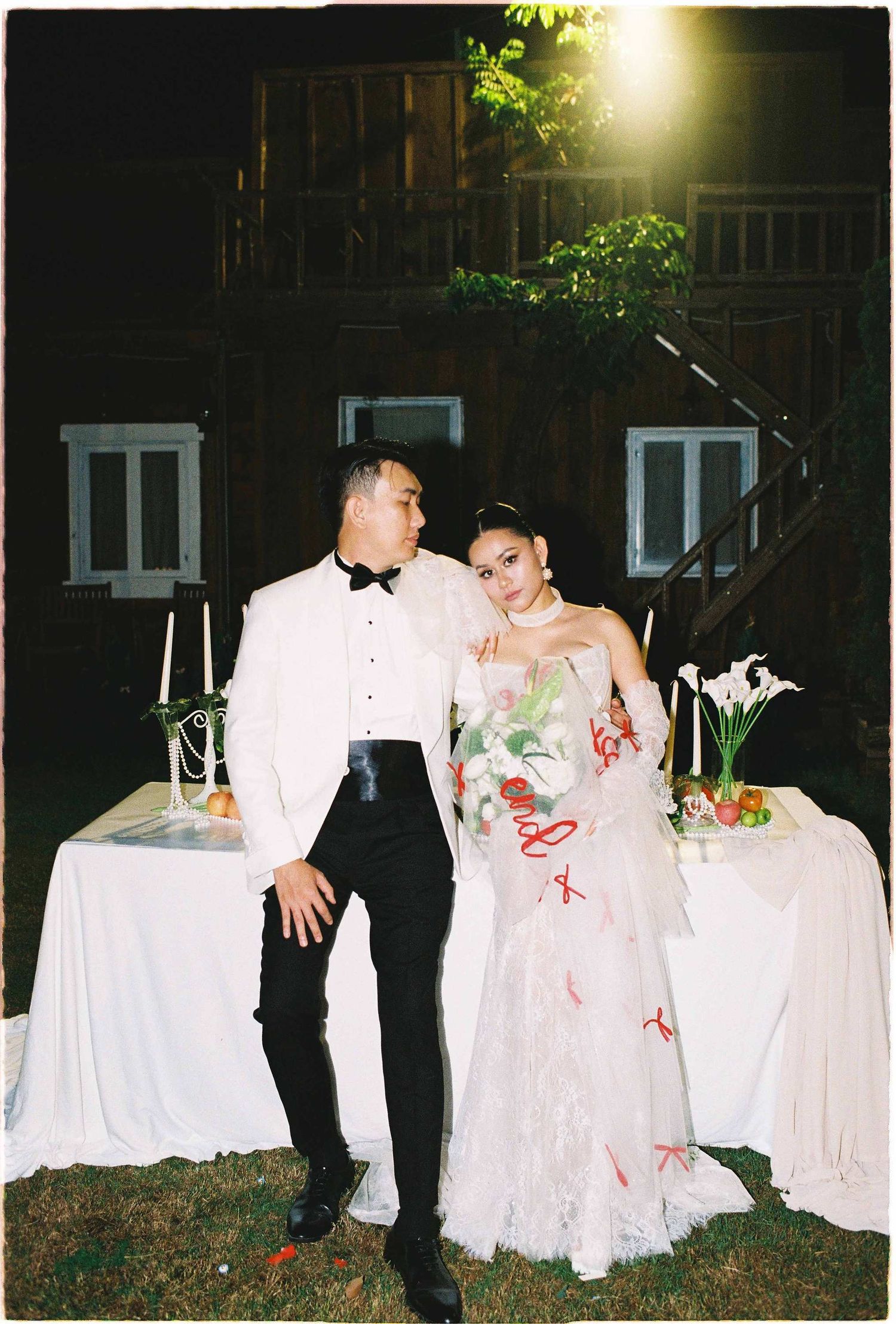 Saigon pre-wedding: wedding couple poses intimately by a decorated white table with floral arrangements at night, by AnhVuWedding.
