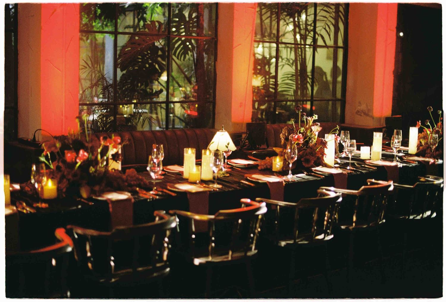 Elegant dimly lit banquet table set for a formal dinner with candles and floral centerpieces in warm red ambient lighting.