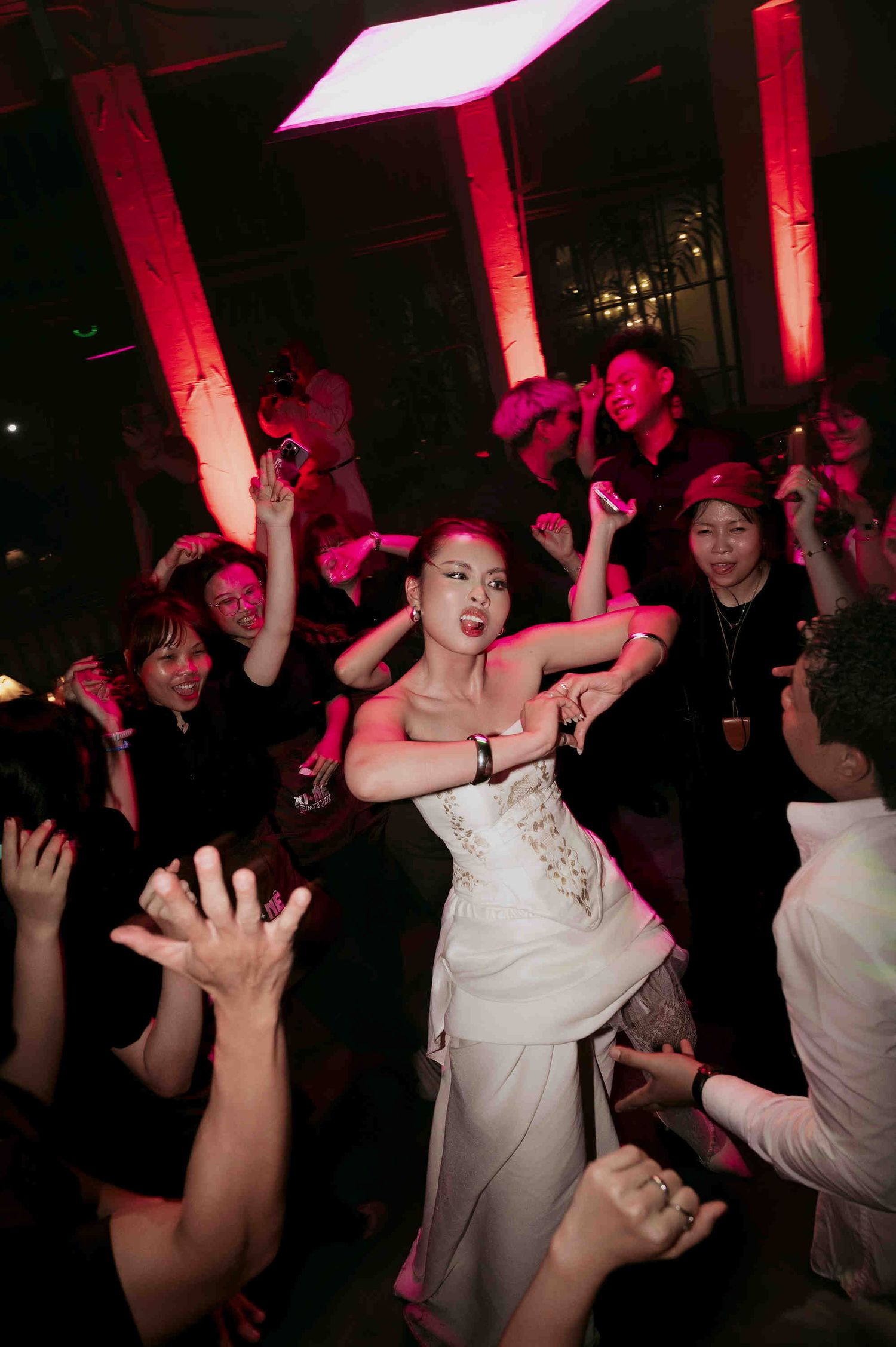 Bride in white wedding dress dancing joyfully surrounded by guests at a lively wedding reception party.