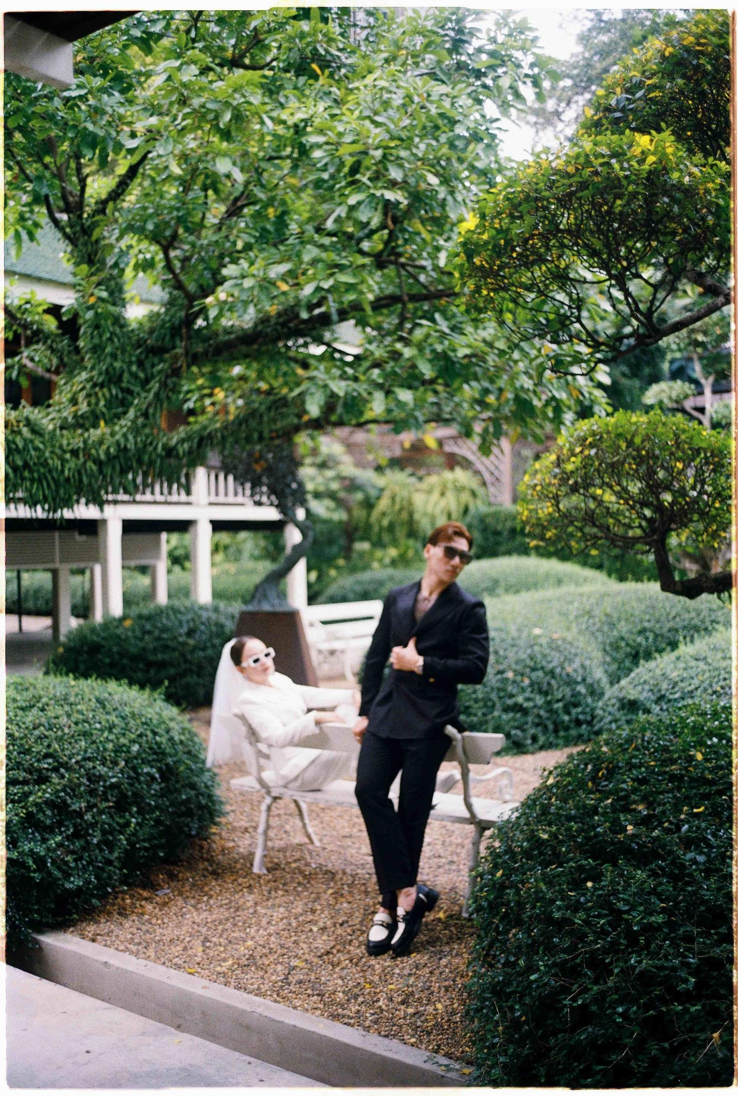 Saigon pre-wedding: garden seating area with white benches surrounded by manicured shrubs and trees, by AnhVuWedding.