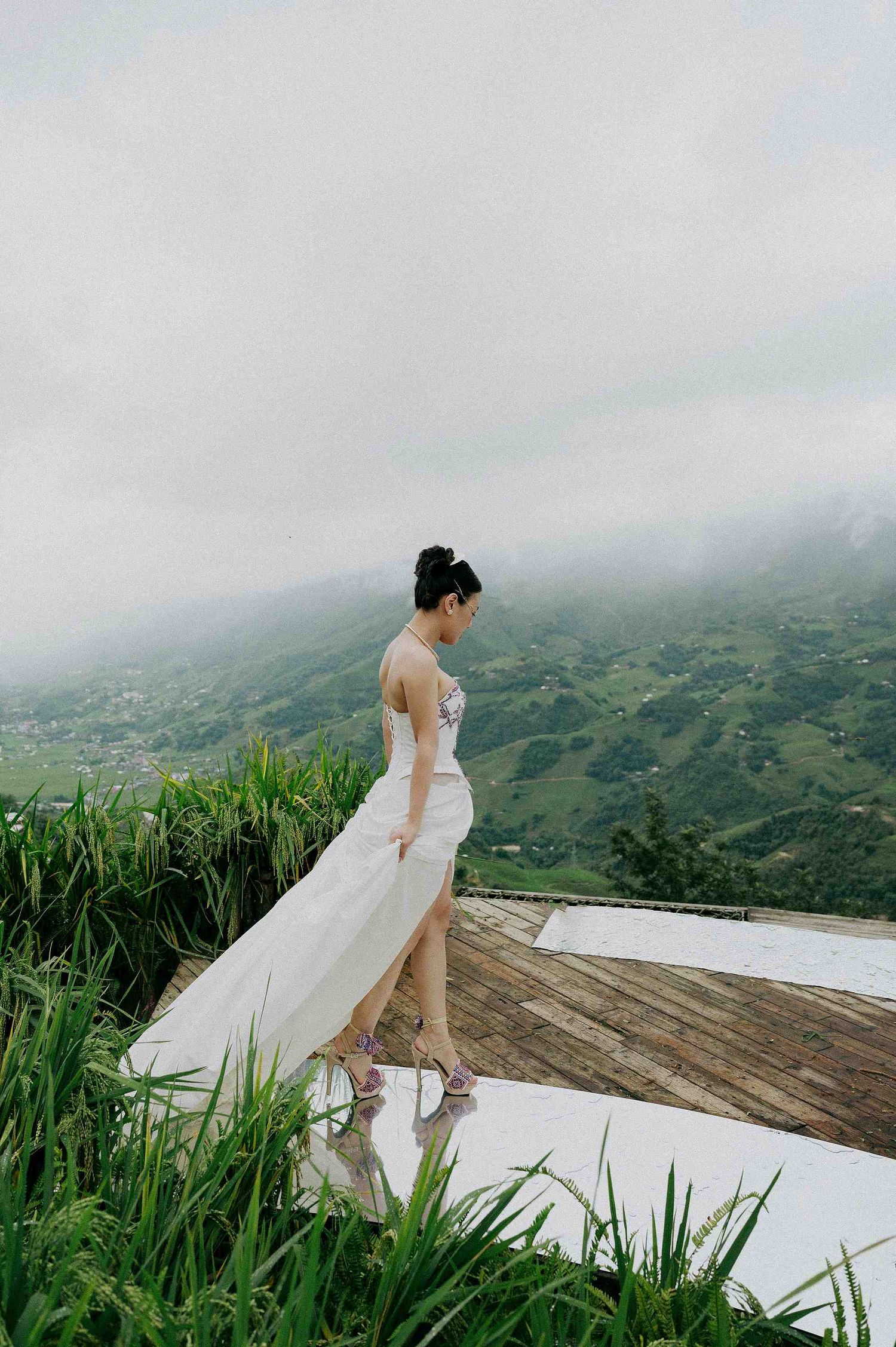 wedding: bride in flowing white dress walks along wooden deck with mountain vista in background, by AnhVuWedding.