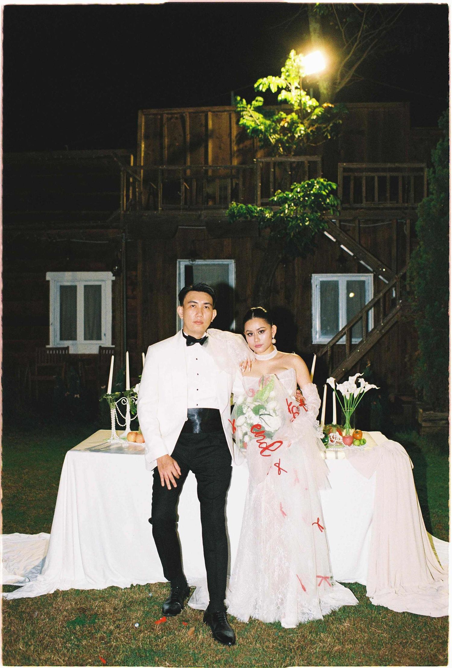 Saigon pre-wedding: wedding couple stands by decorated tables outdoors at night with white linens and floral arrangements, by AnhVuWedding.
