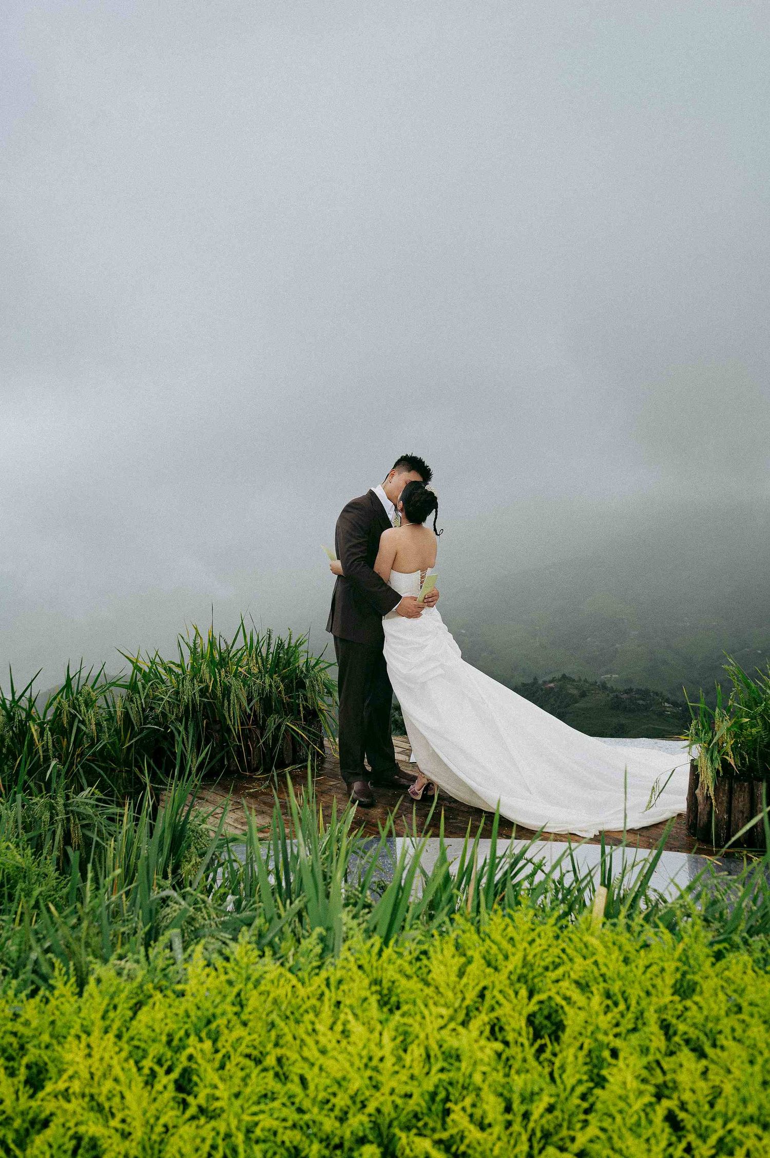 wedding: couple in wedding attire poses in a field of tall grass and yellow flowers with a misty background, by AnhVuWedding.