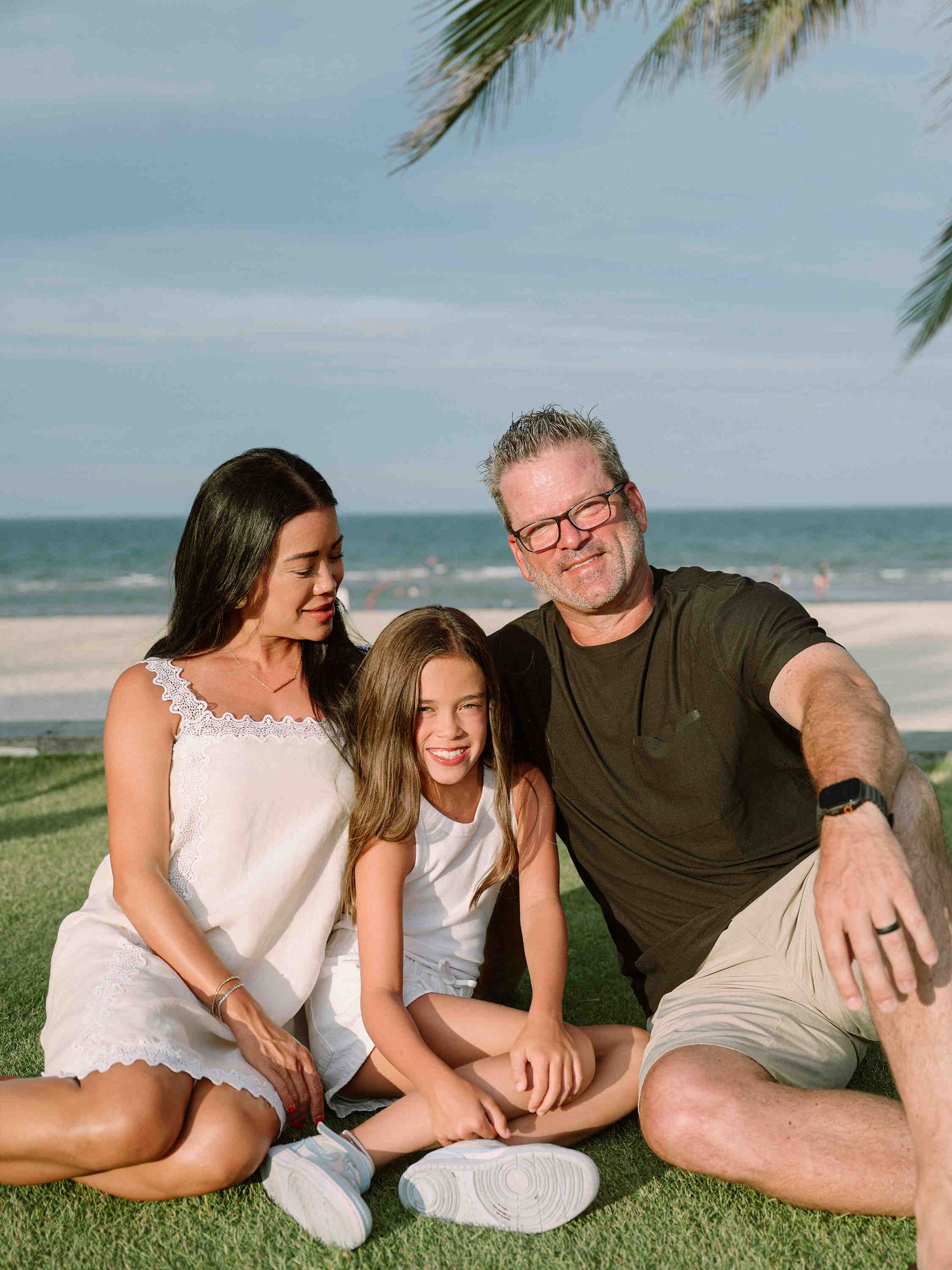 Da Nang family: family relaxes together on grass near a beach on a sunny day, captured in a series of candid moments, by AnhVuWedding.