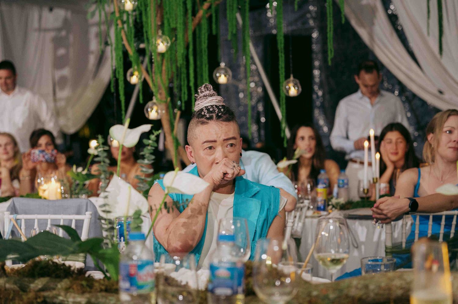 Man wearing a party hat blowing a noisemaker at a festive outdoor celebration with decorated tables.
