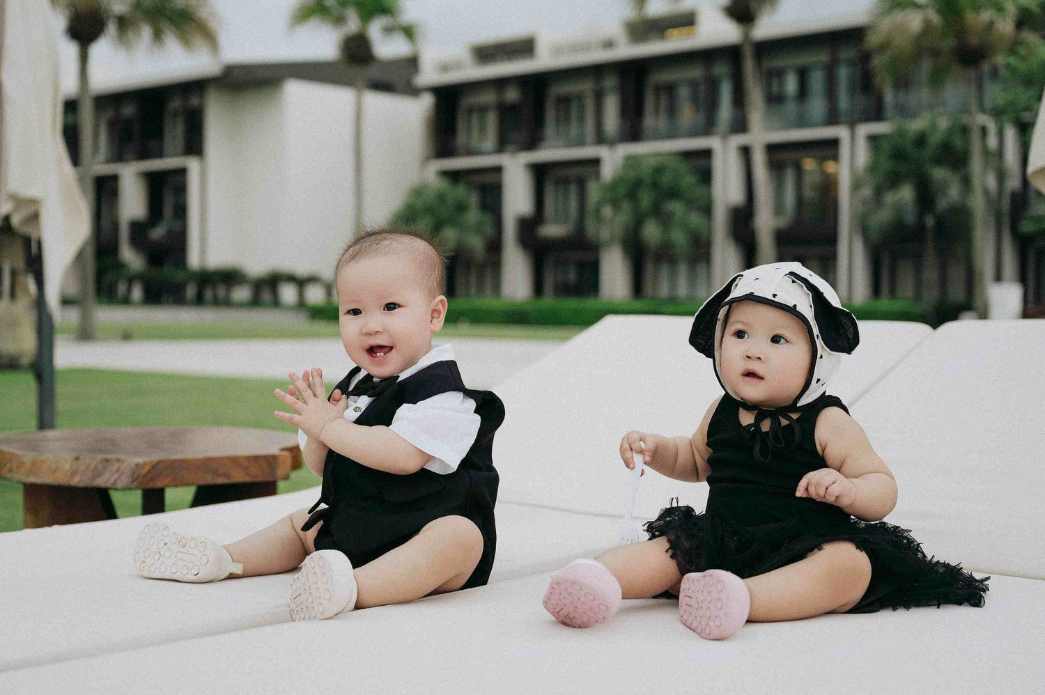 Da Nang family: babies in black outfits lying on white cushions outdoors, by AnhVuWedding.