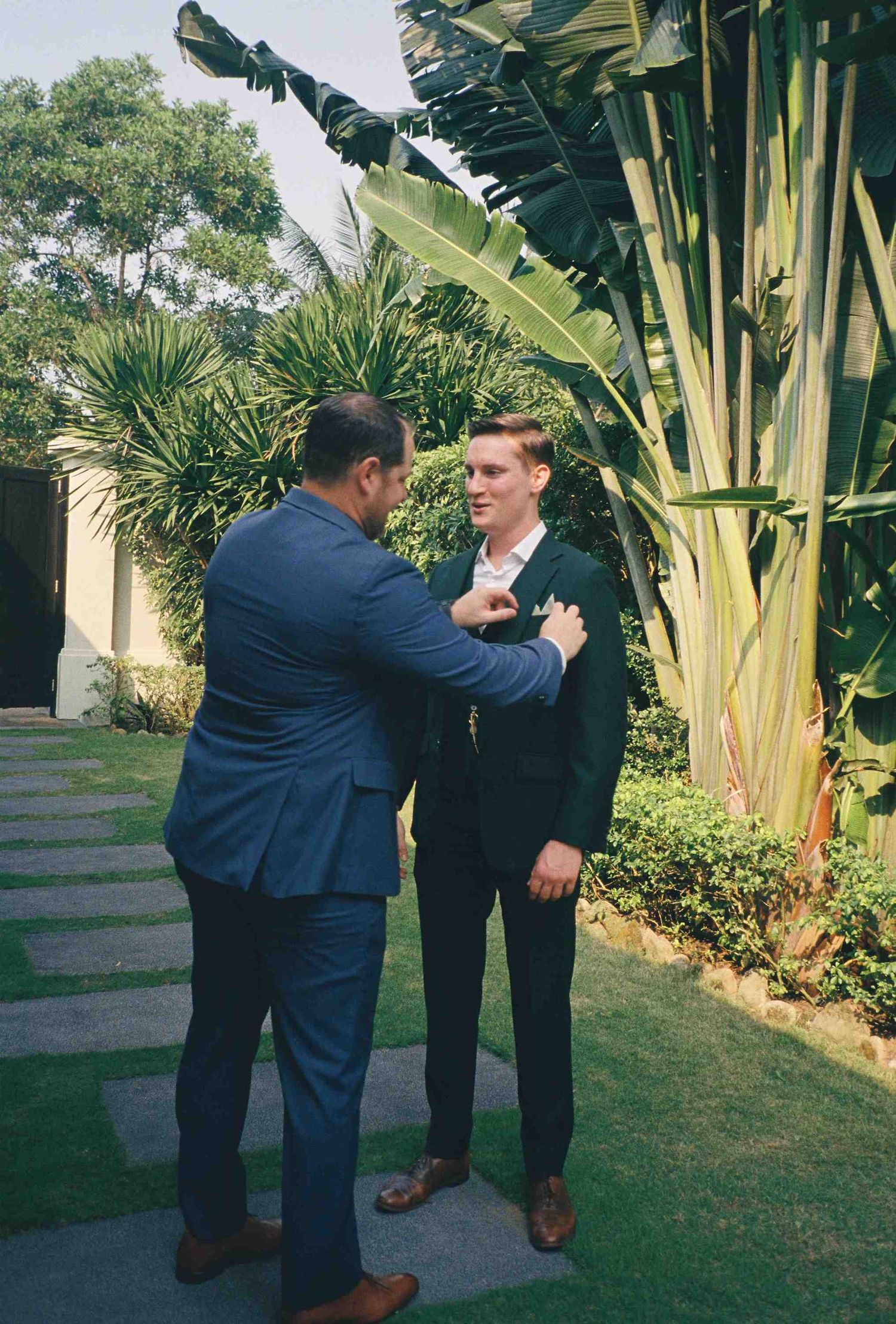 Lang Co wedding: two men in suits adjust clothing outdoors, by AnhVuWedding.