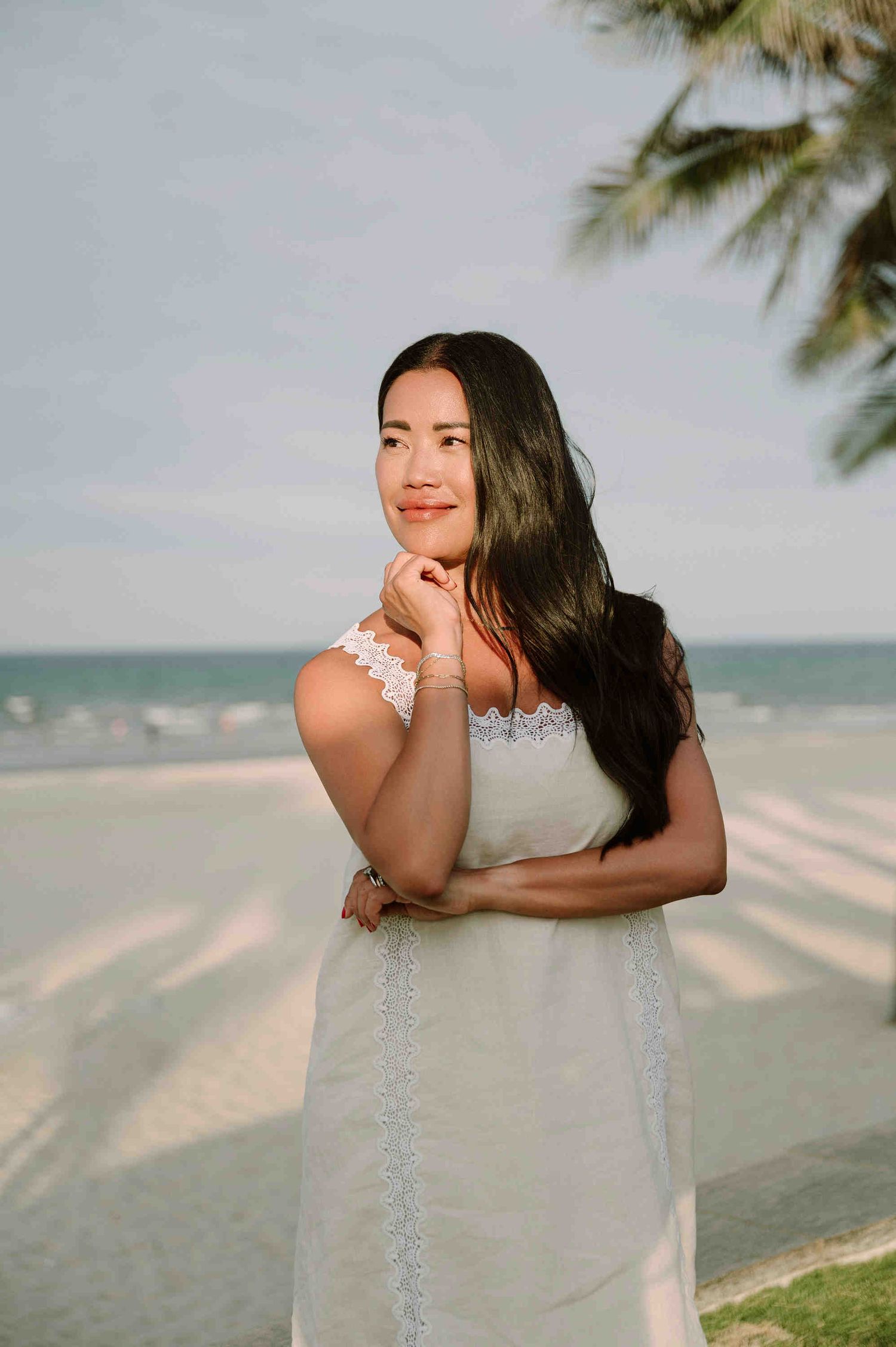 Da Nang family: woman in a white lace dress poses on a tropical beach, by AnhVuWedding.