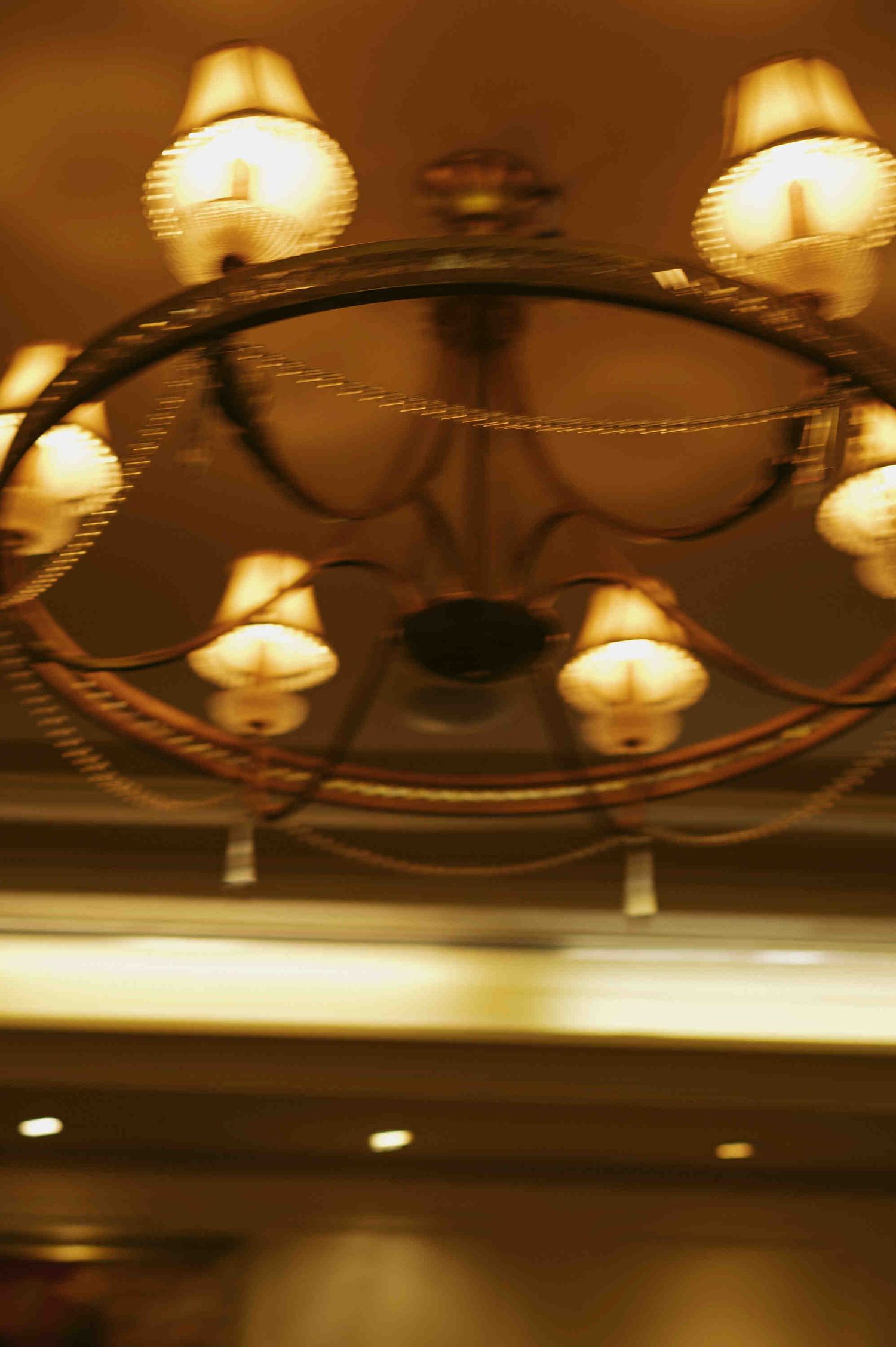 Elegant circular chandelier with warm glowing candle-style lights hanging from an ornate ceiling in a luxurious interior.