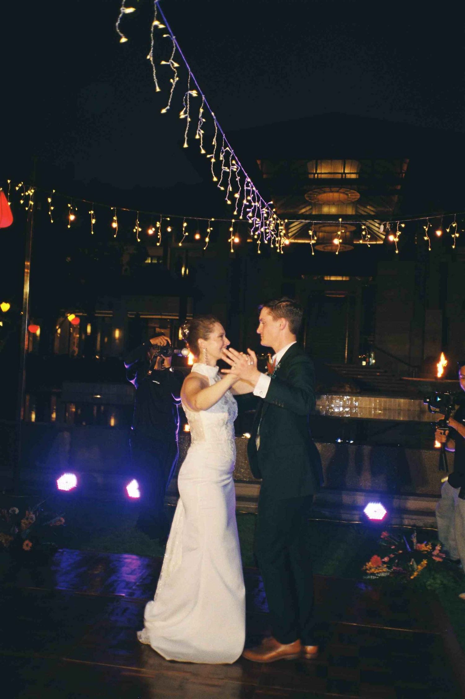 Lang Co wedding reception: couple dancing at an outdoor wedding reception with purple lighting and string lights overhead, by AnhVuWedding.