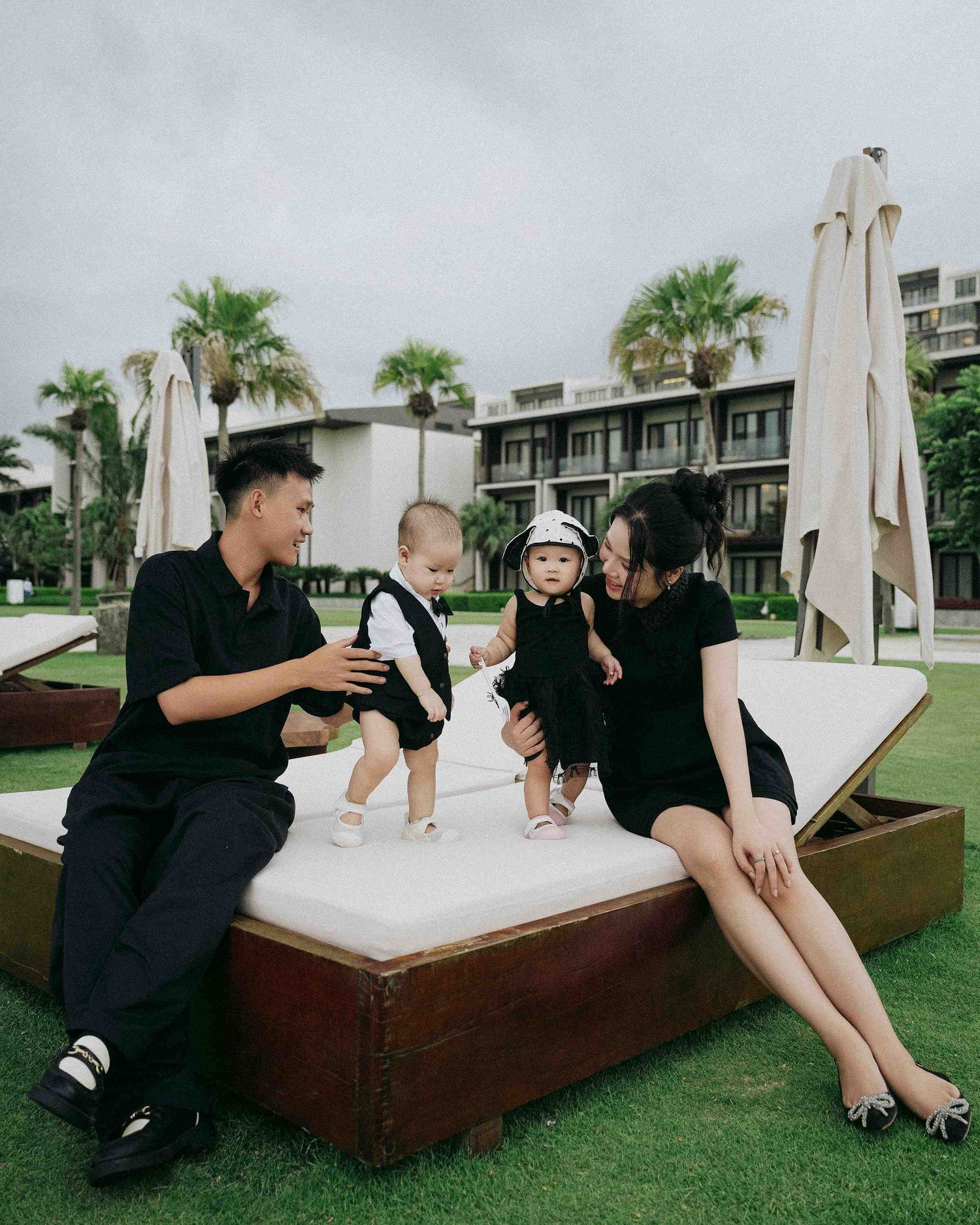 Da Nang family: family enjoying moments together on a wooden daybed with white cushions in a resort setting, by AnhVuWedding.