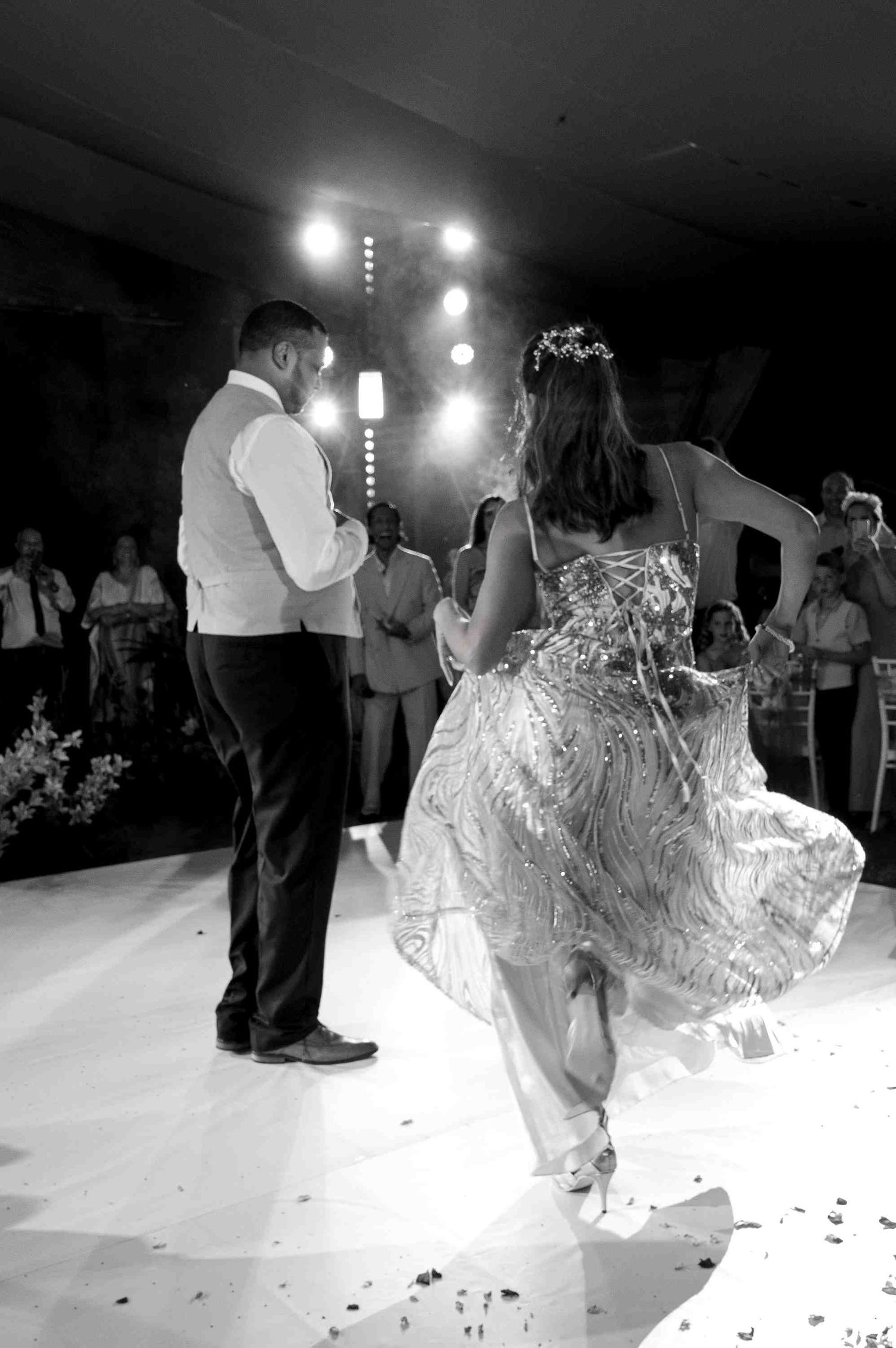 Black and white photo of a bride and groom sharing their first dance at a wedding reception with guests watching.