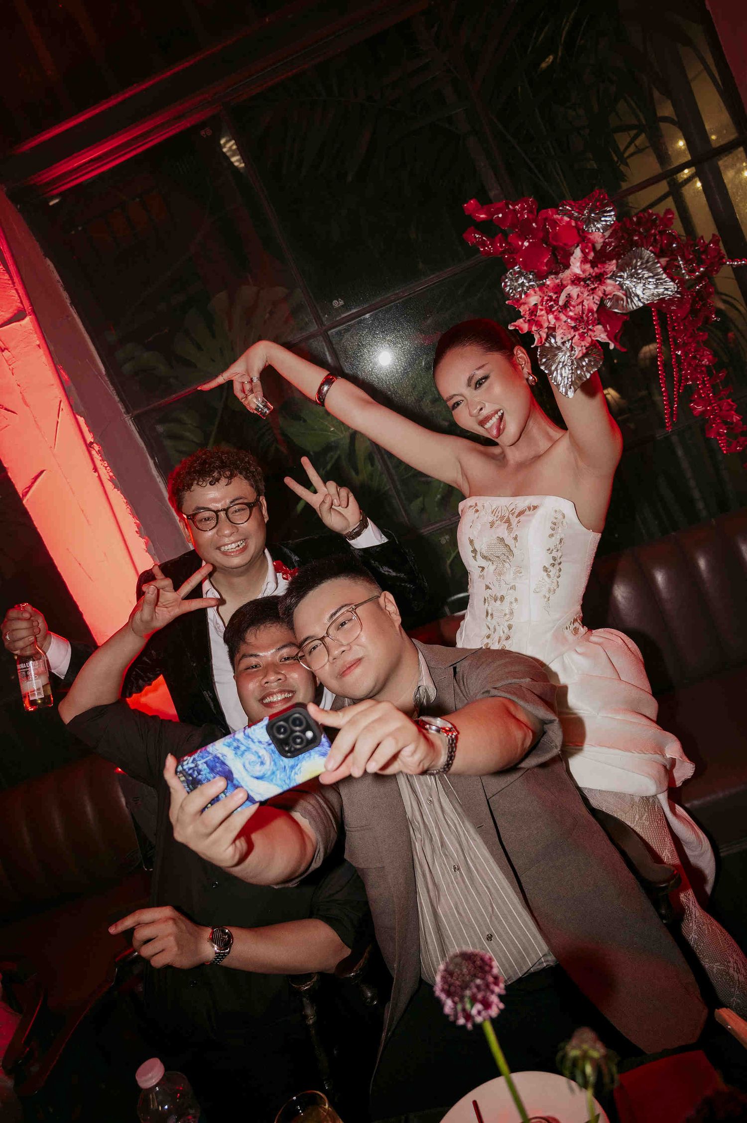 Group of four people posing for a selfie at a nightclub event, with a woman in a white corset and floral headpiece.
