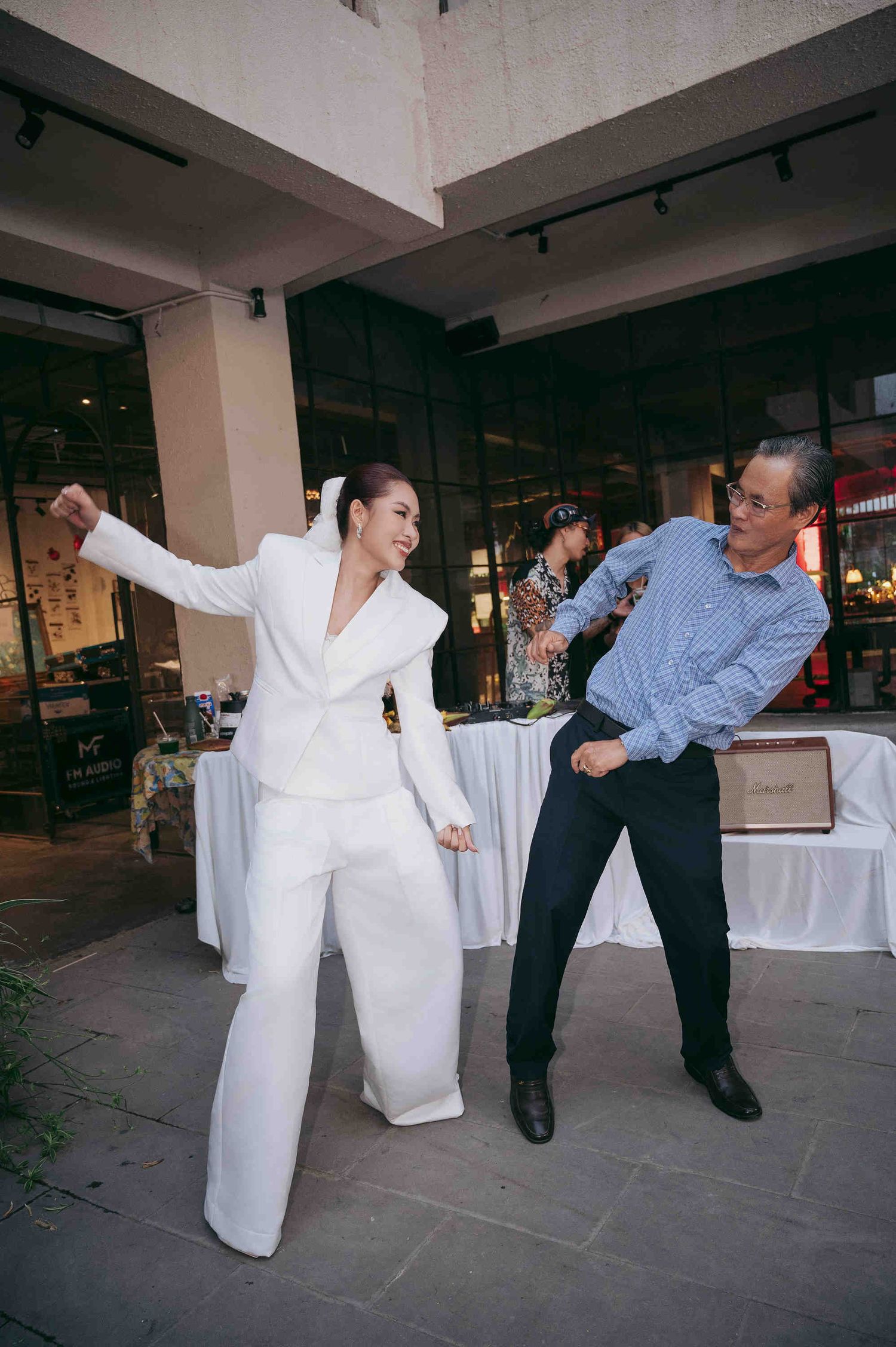 Two people dancing joyfully outdoors, woman in white pantsuit and man in blue striped shirt at a social event.