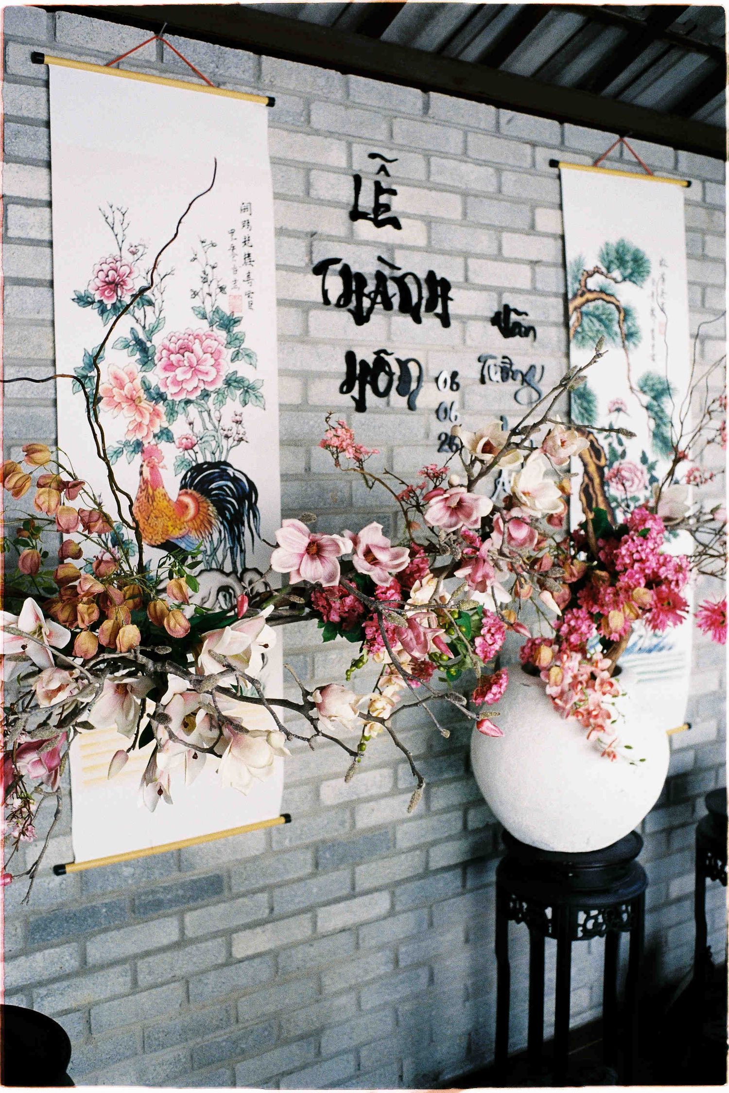 Vietnamese wedding scrolls with floral arrangements featuring pink blooms and calligraphy on a brick wall backdrop.