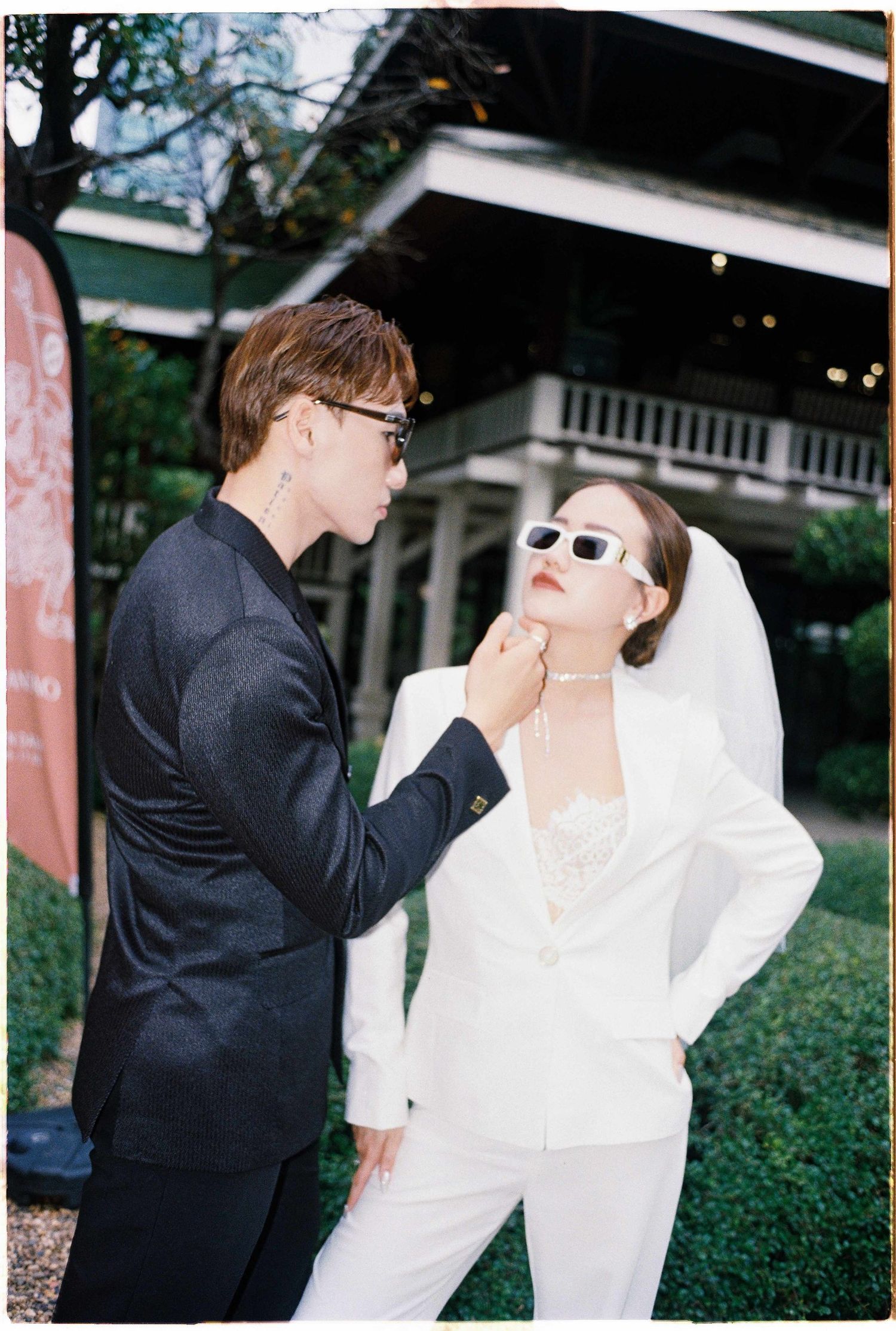 Saigon pre-wedding: couple in sunglasses and monochromatic outfits interact dramatically in a garden setting, by AnhVuWedding.