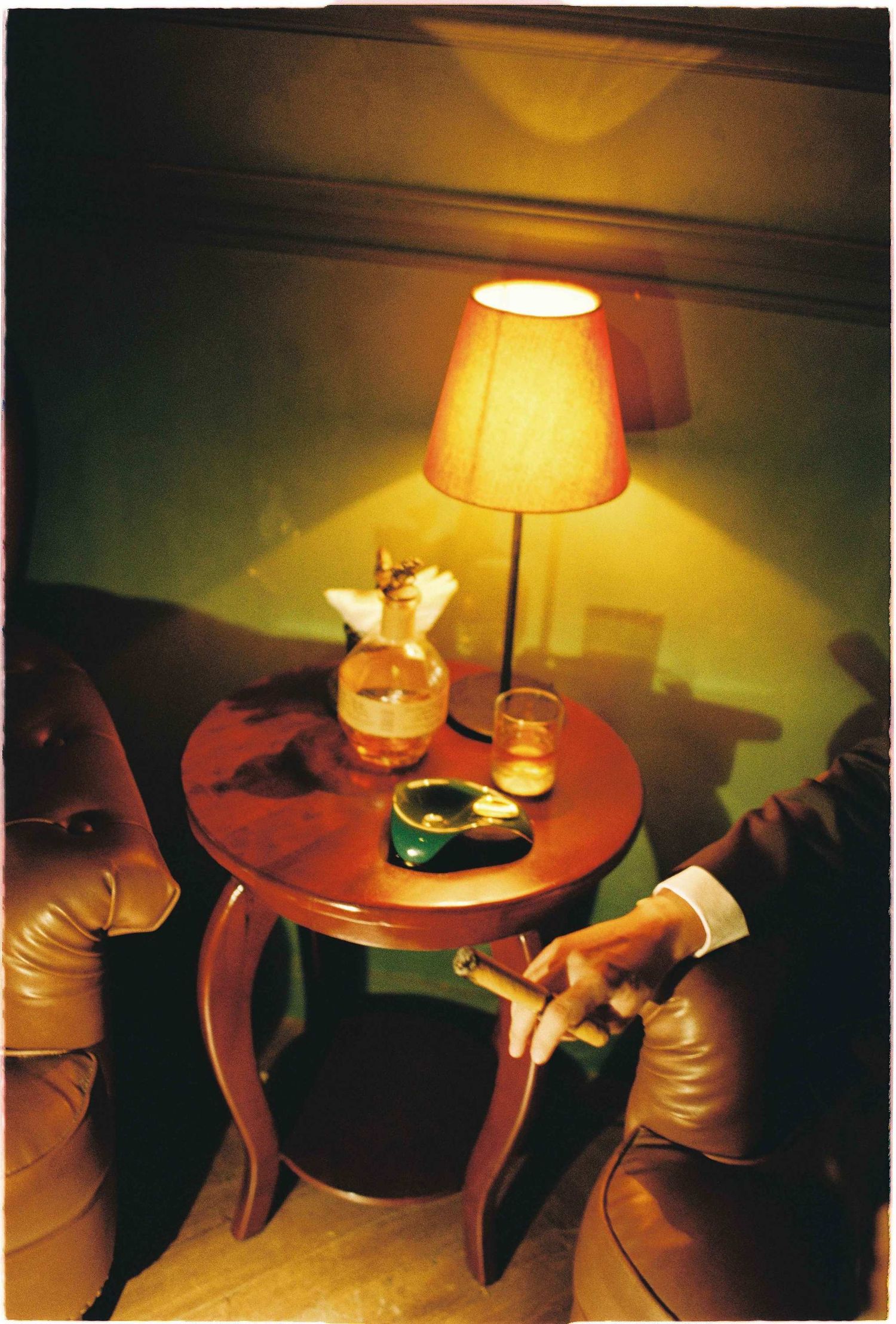 Vietnam pre-wedding: table lamp illuminates a cozy corner with drinks and an ashtray on a round wooden side table, by AnhVuWedding.