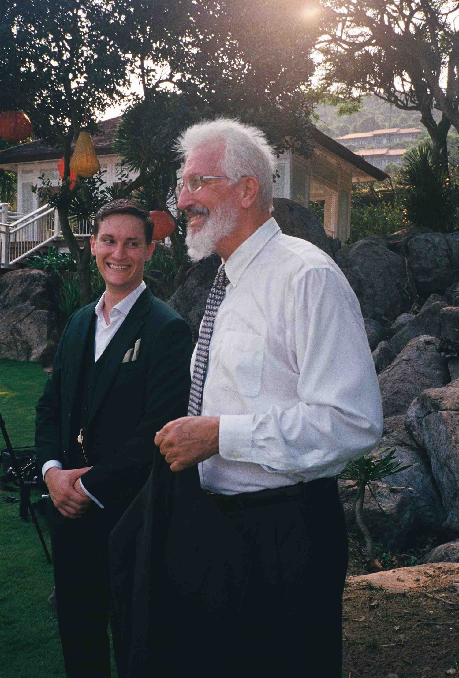 Lang Co wedding: wedding guests in formal attire sharing laughs on outdoor garden path at dusk, by AnhVuWedding.