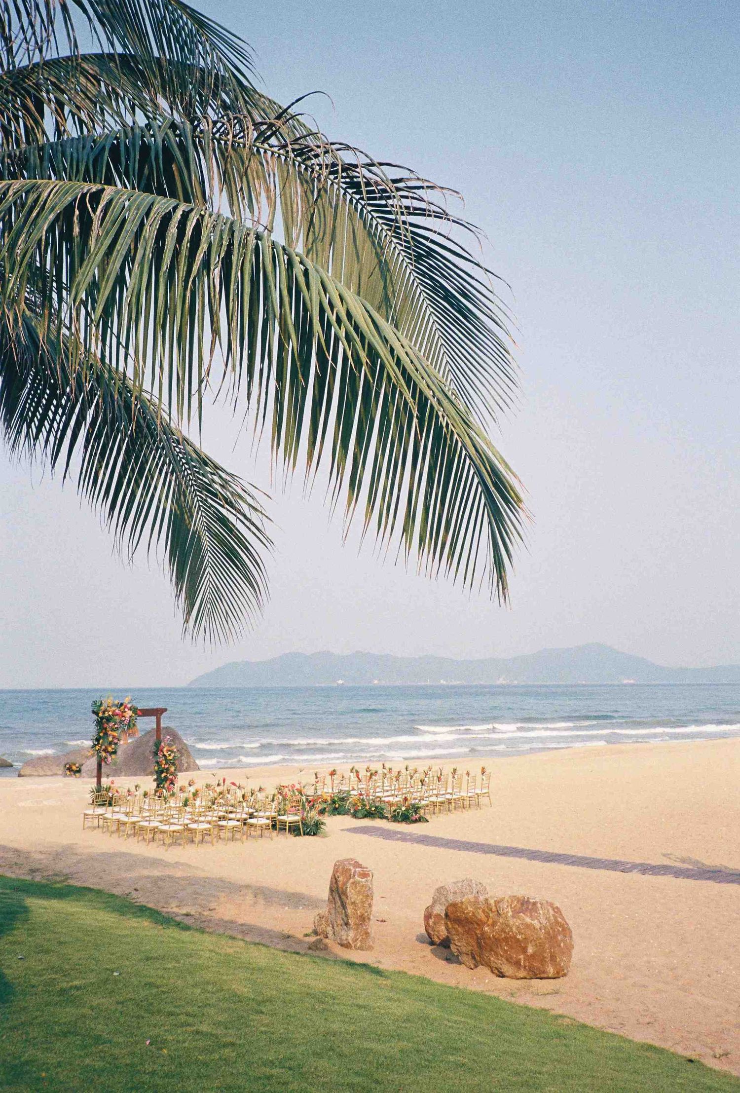 Lang Co wedding: tropical beach landscape with palm trees and mountains in the distance on a clear sunny day, by AnhVuWedding.