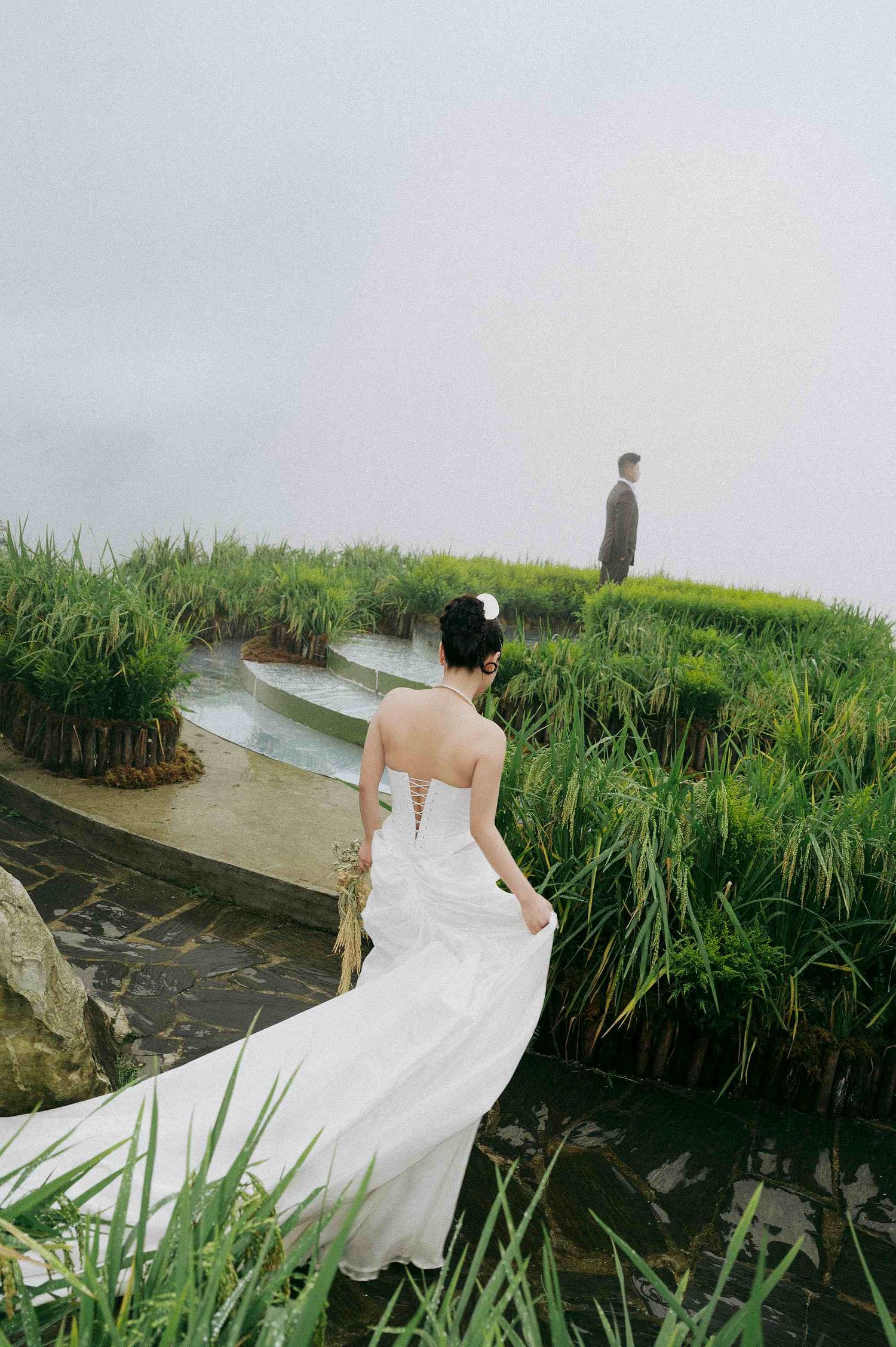 wedding: bride in a white dress poses near tall grasses and water in an ethereal outdoor setting, by AnhVuWedding.