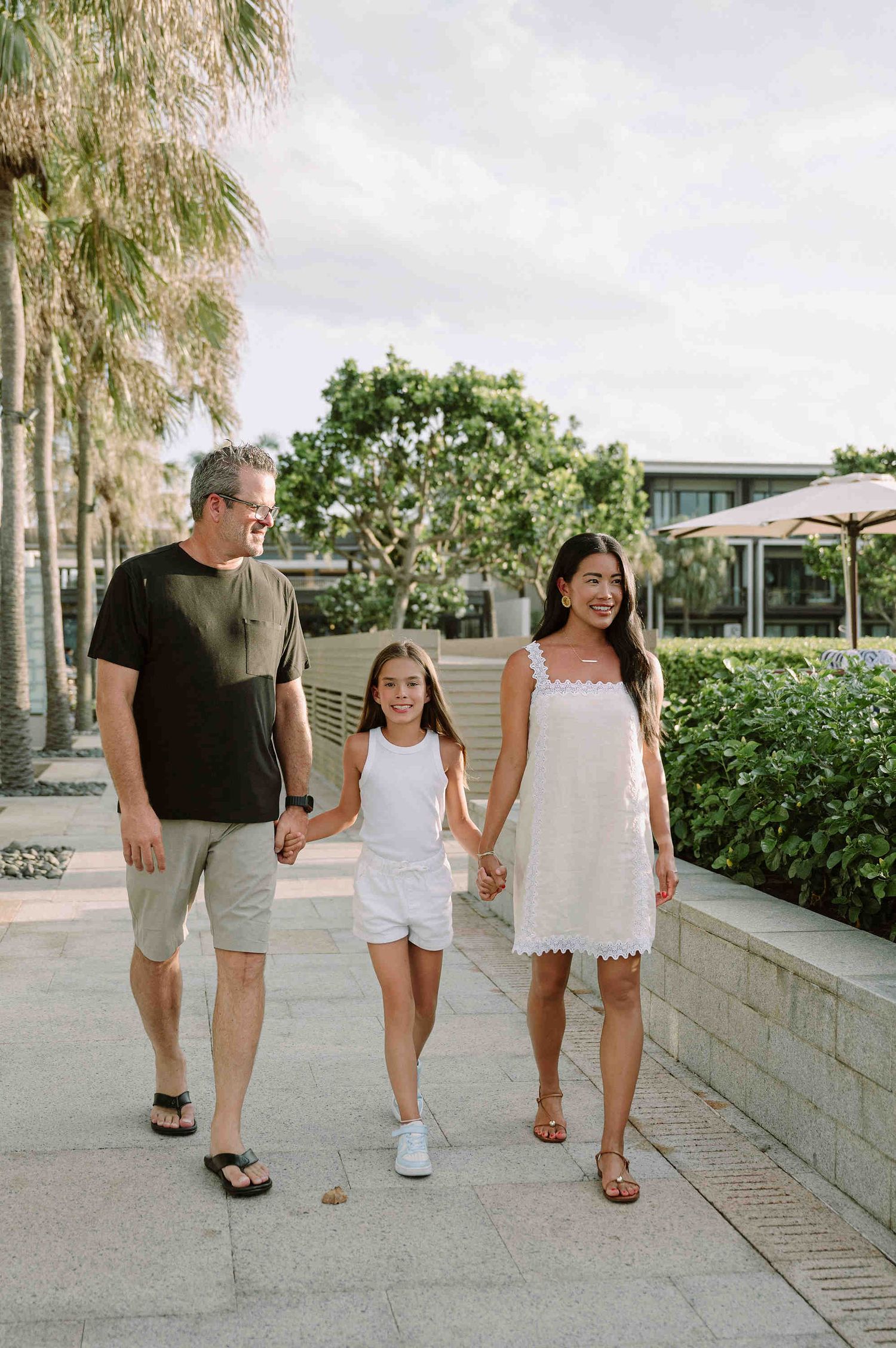 Da Nang family: family walks together along a palm-lined pathway on a sunny afternoon, by AnhVuWedding.