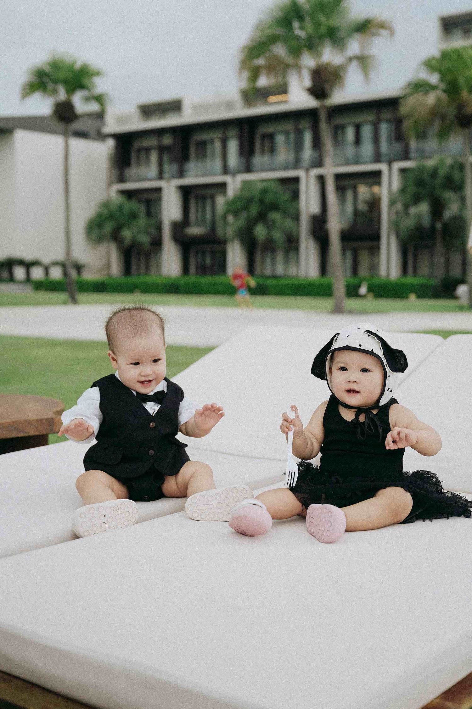 Da Nang family: infants in black outfits lying on a white surface, by AnhVuWedding.