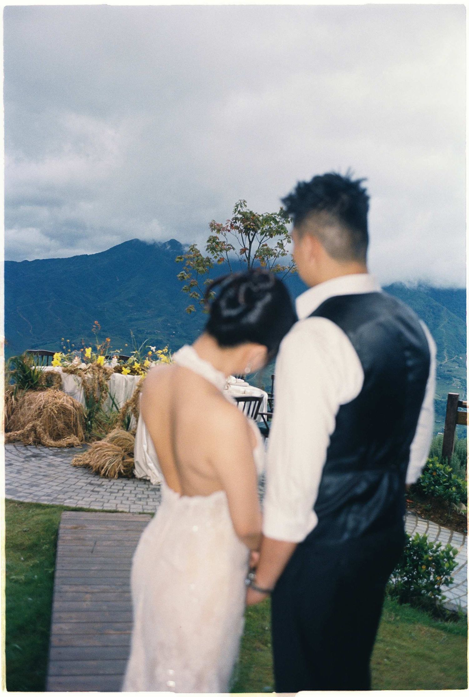 wedding: couple in wedding attire walking along a stone path with mountain views, by AnhVuWedding.