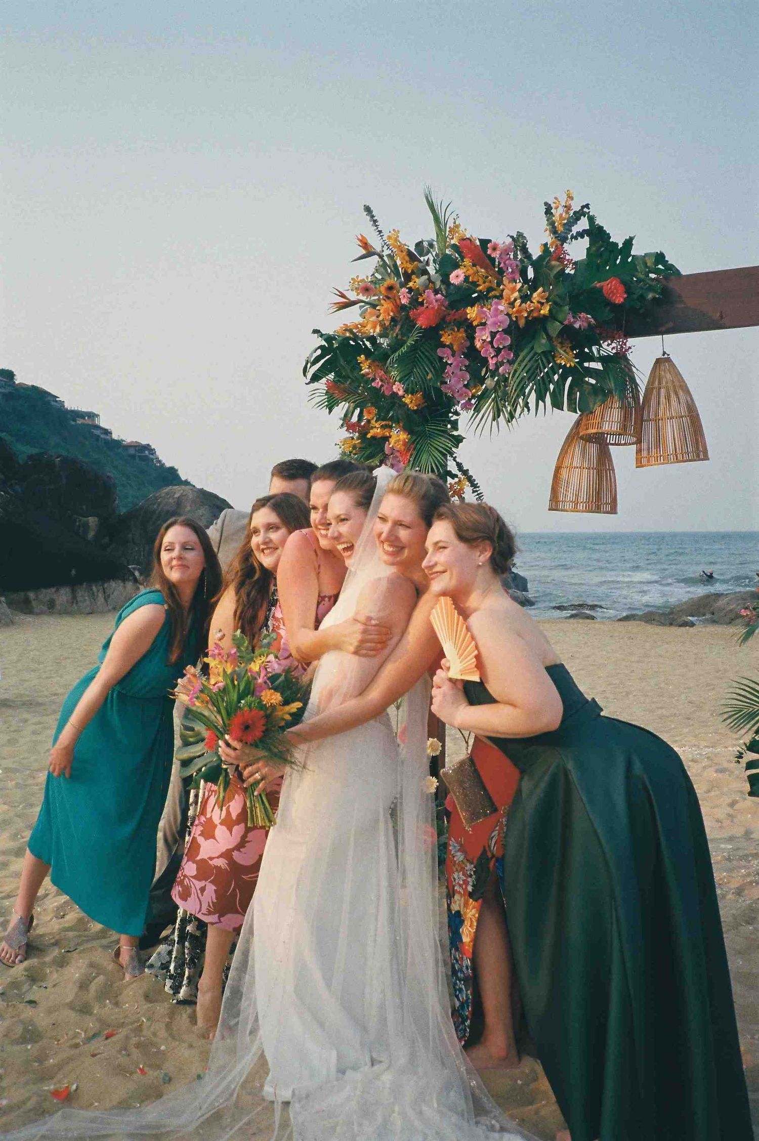 Lang Co wedding: bridal party embraces for casual group photo on beach with tropical decor, by AnhVuWedding.