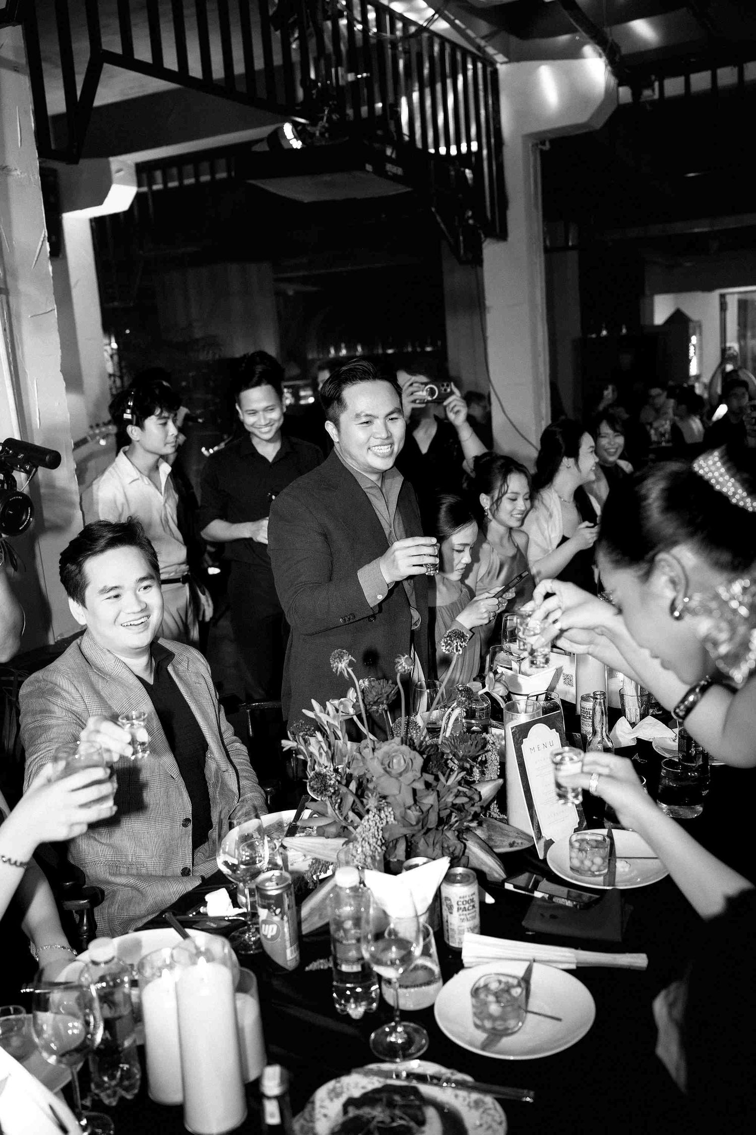Black and white photo of elegantly dressed guests toasting drinks at a formal dinner party event.