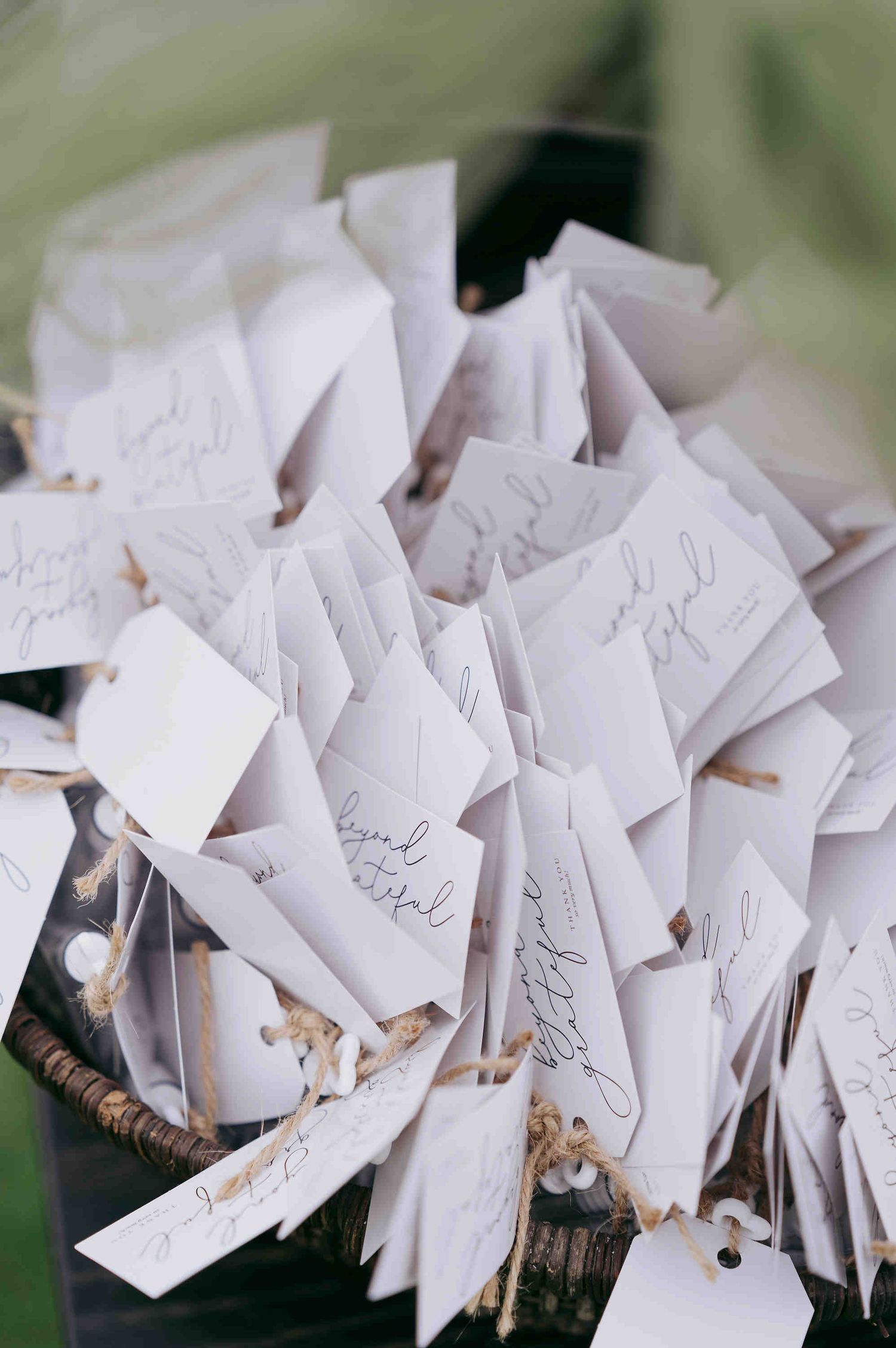 White escort cards with handwritten calligraphy tied with twine, displayed in a rustic basket for a wedding reception.