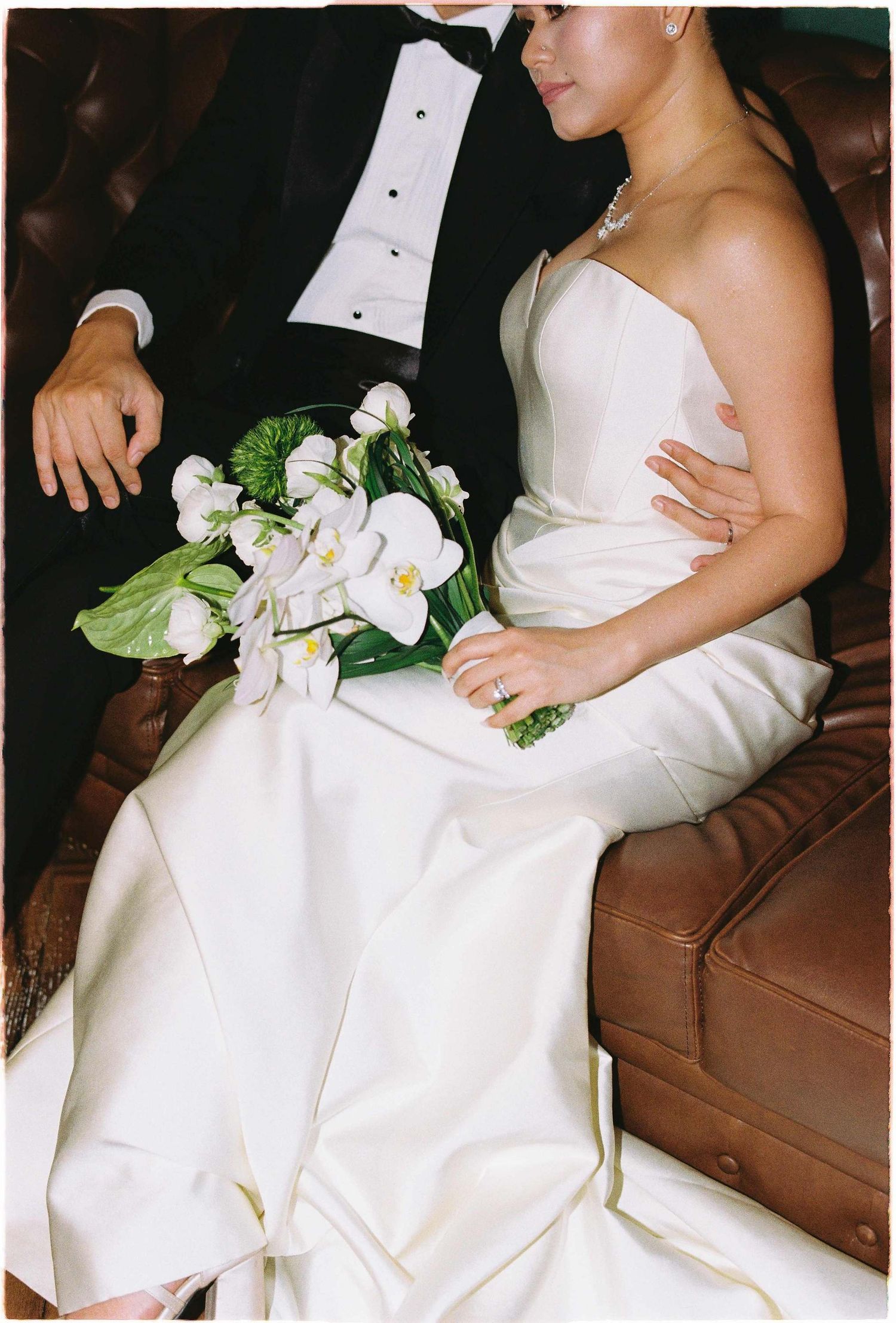 Vietnam pre-wedding: wedding couple seated on leather couch with white floral bouquet, by AnhVuWedding.