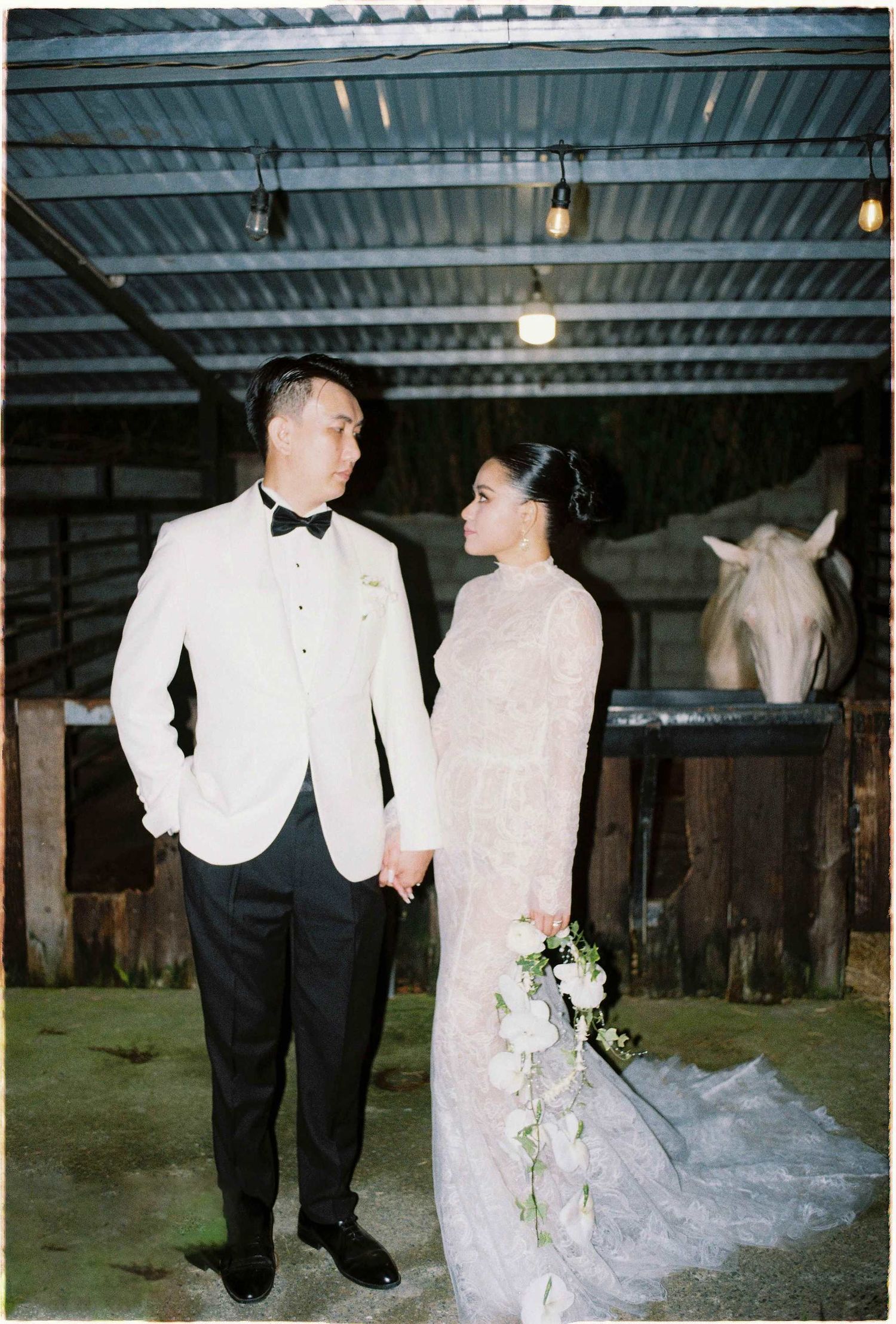 Saigon pre-wedding: couple in formal attire walking through a rustic horse stable, by AnhVuWedding.