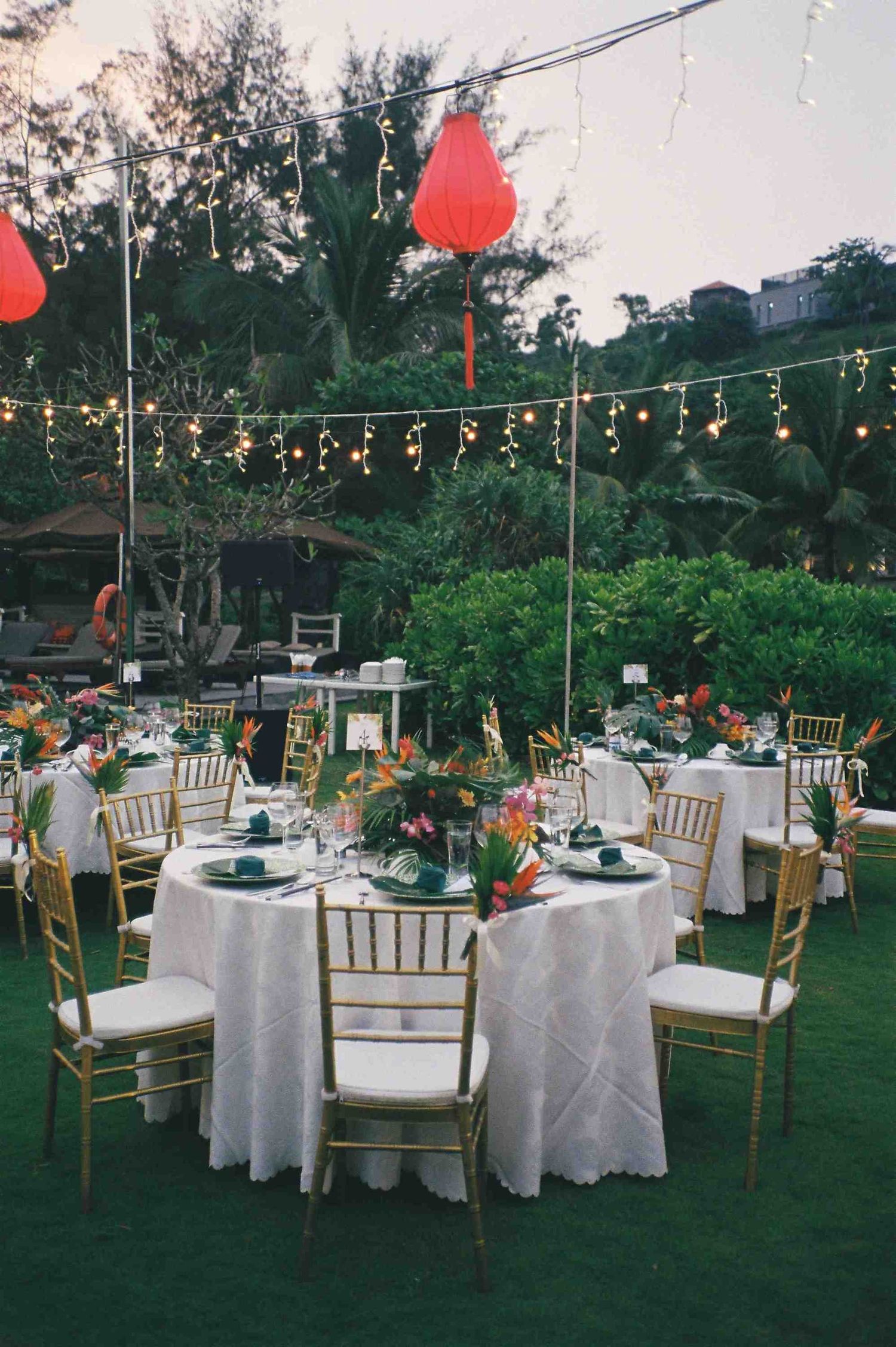 Lang Co wedding reception: outdoor wedding reception setup with white tables, gold chairs and string lights under evening, by AnhVuWedding.
