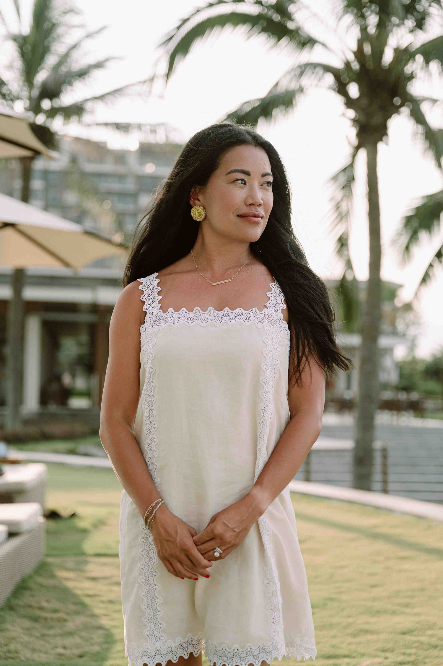 Da Nang family: person in a white lace dress stands in a tropical setting with palm trees and grass, by AnhVuWedding.
